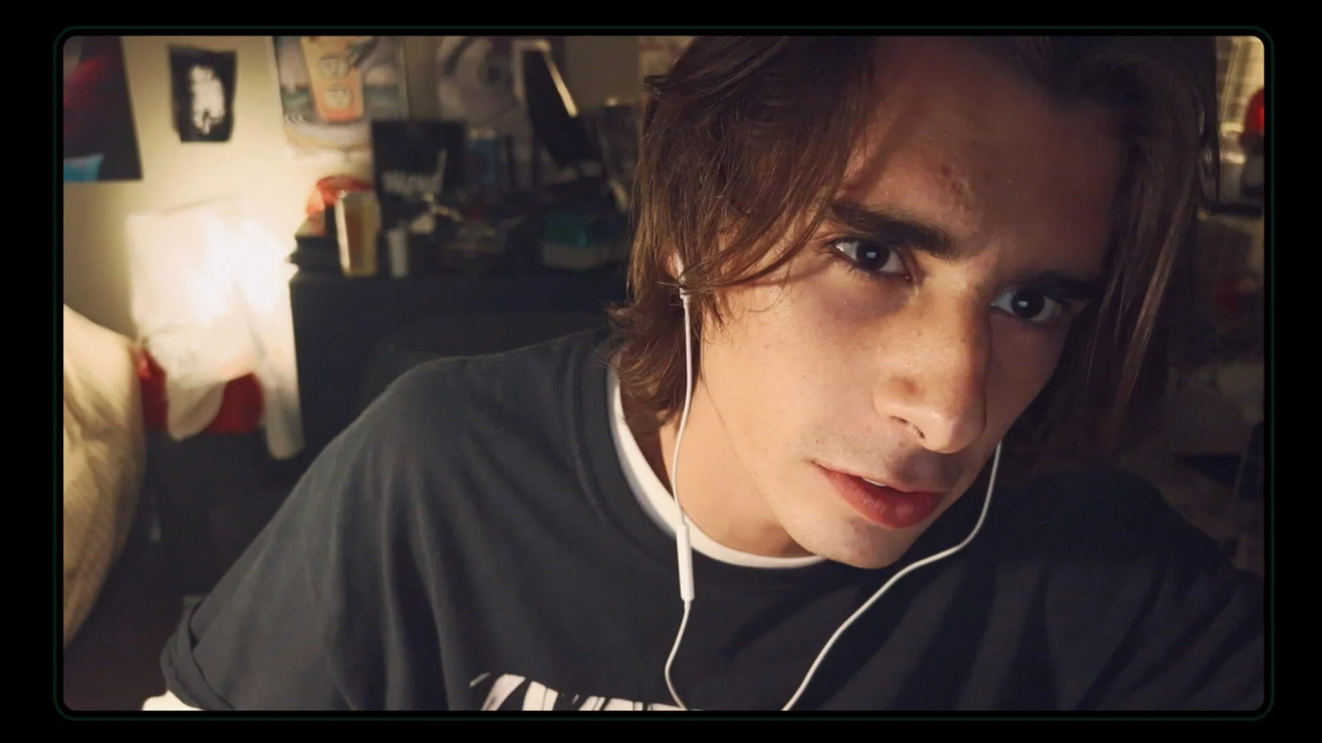 Kyle wears white earbuds in a dimly lit bedroom.