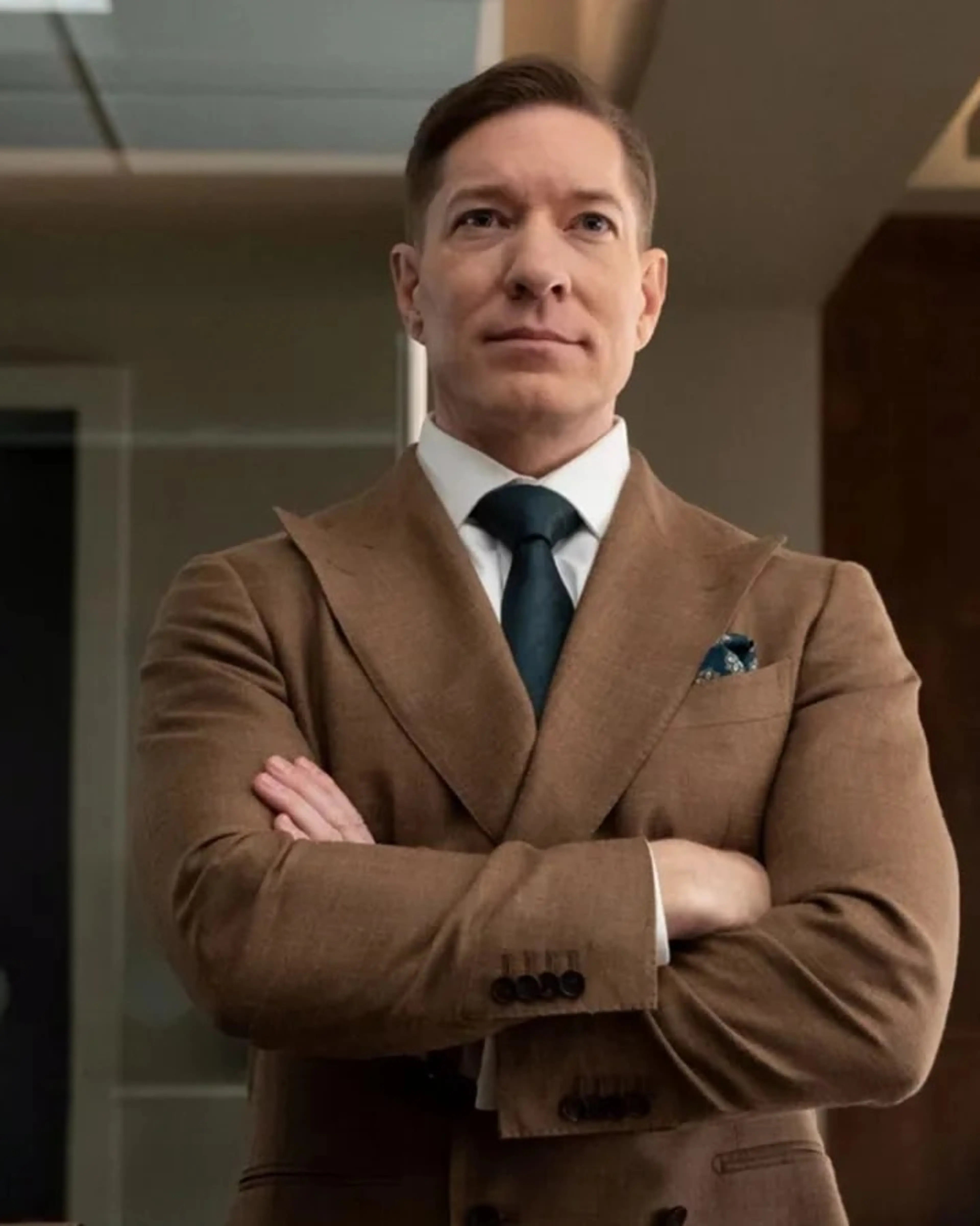 Joseph Sikora as Bill Sterling stands in an office in a brown suit.