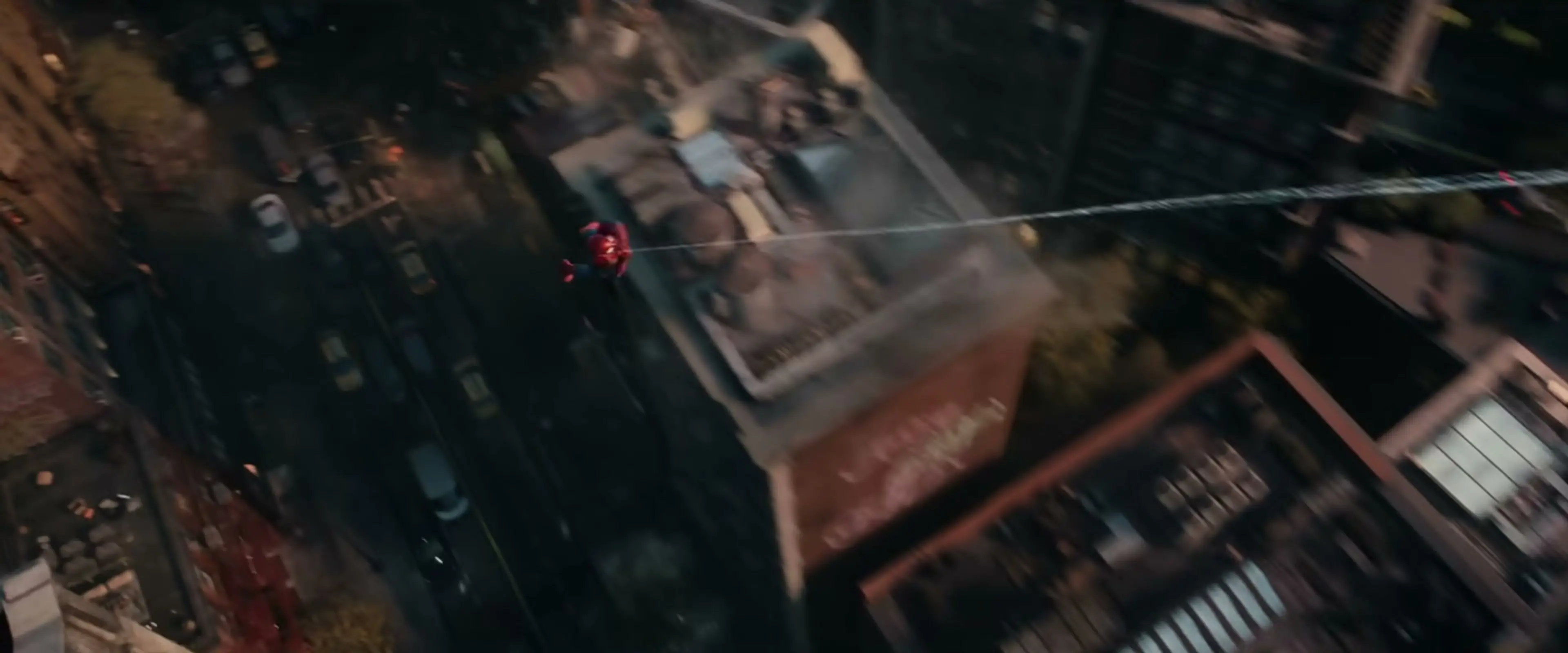Spider-Man swings on a web over a New York street, seen from above.