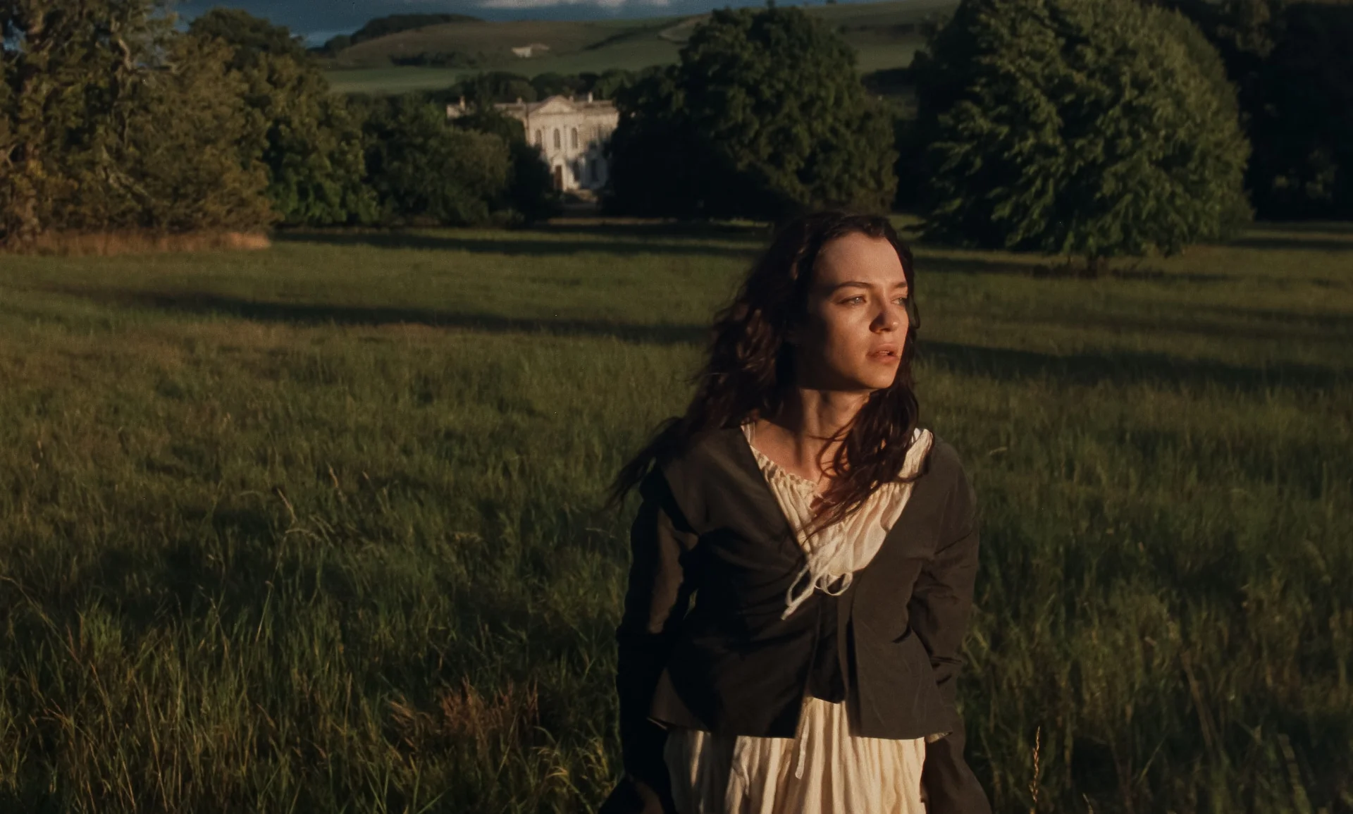 Marianne stands in long grass with a large country house behind her.