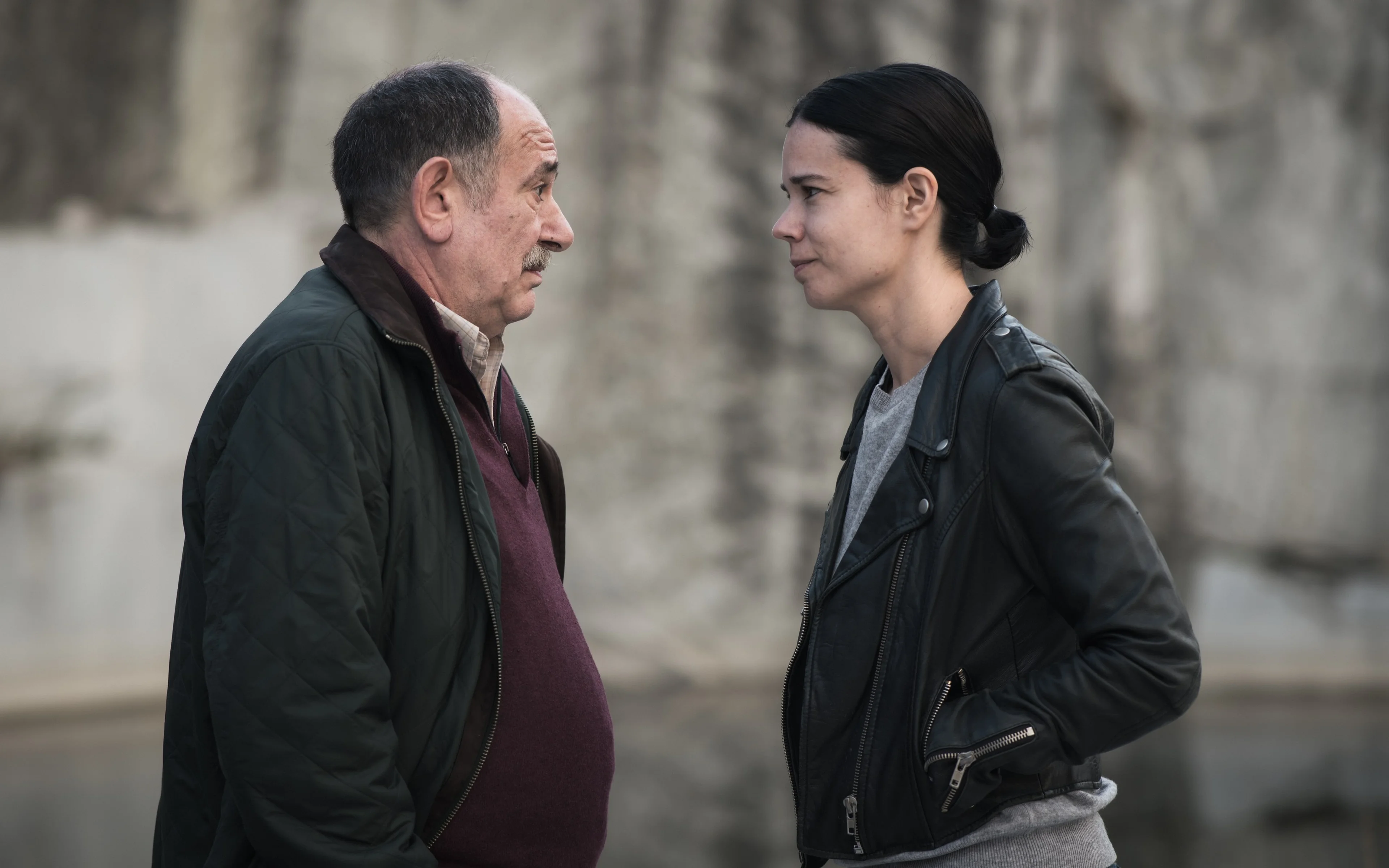 A man and woman face each other outdoors.