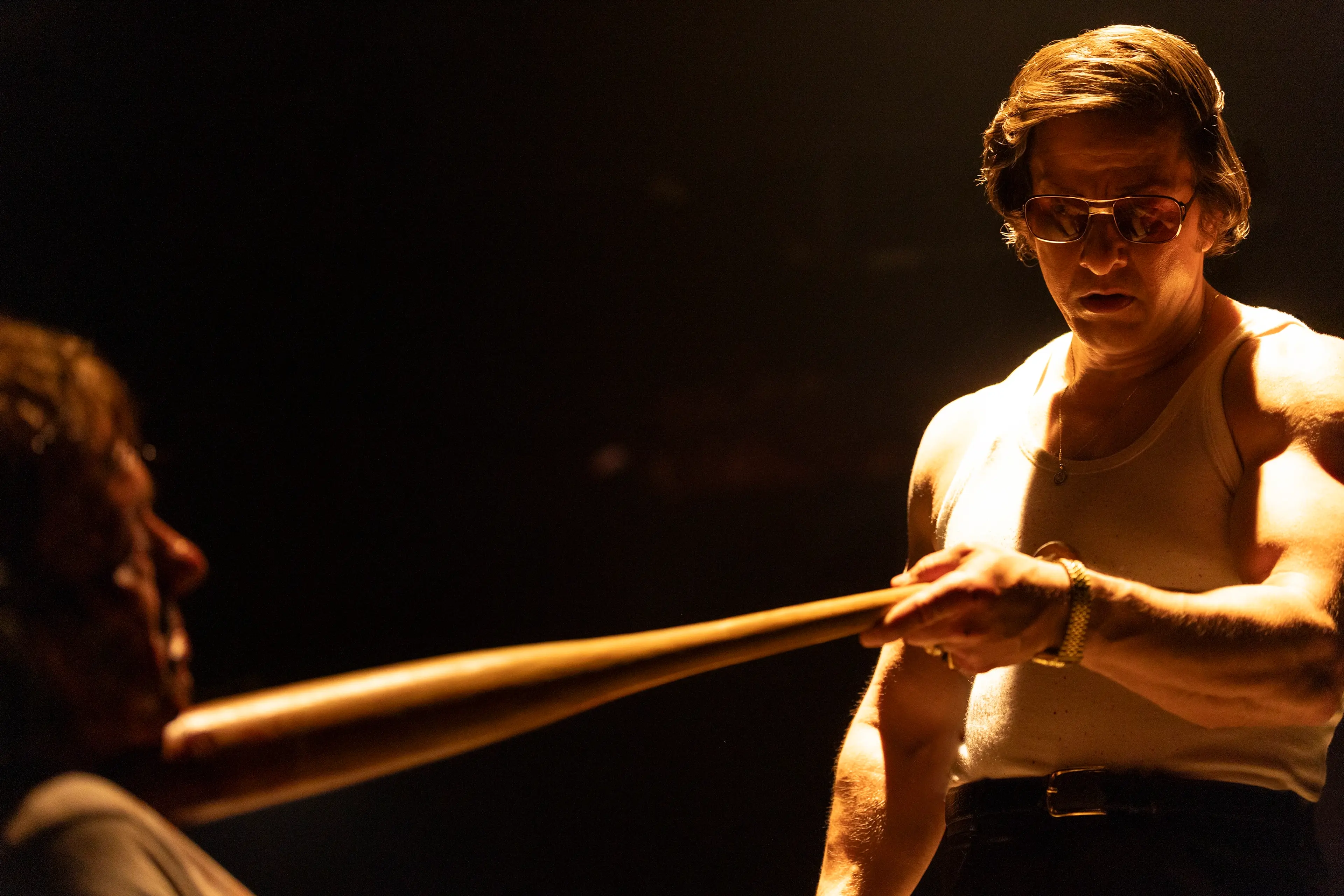 Greg Scarpa points a wooden baseball bat toward a seated man in By Any Means.