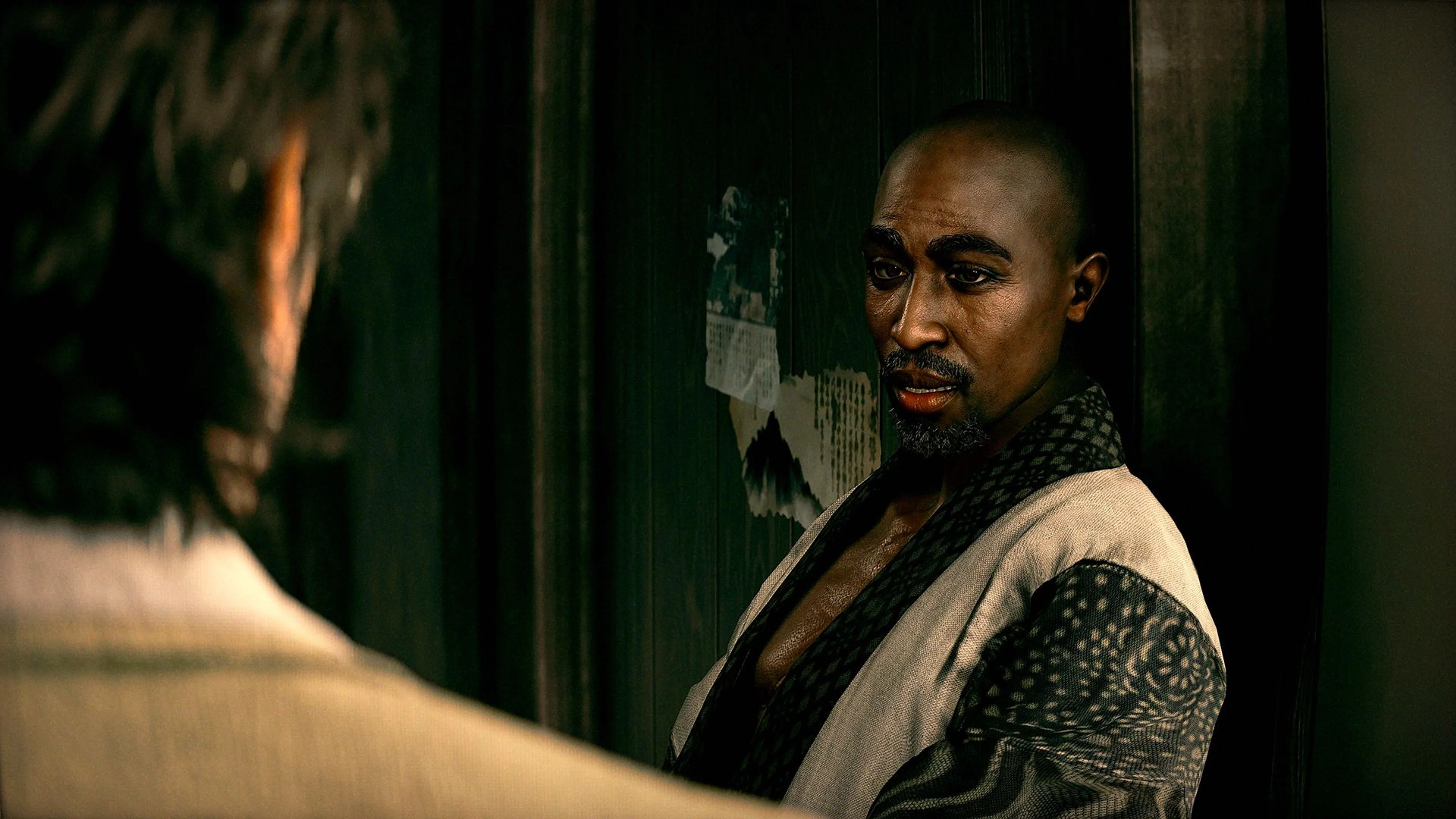 Amaru, the Stranger Than Heaven character based on Tupac Shakur, speaks inside a dim room.