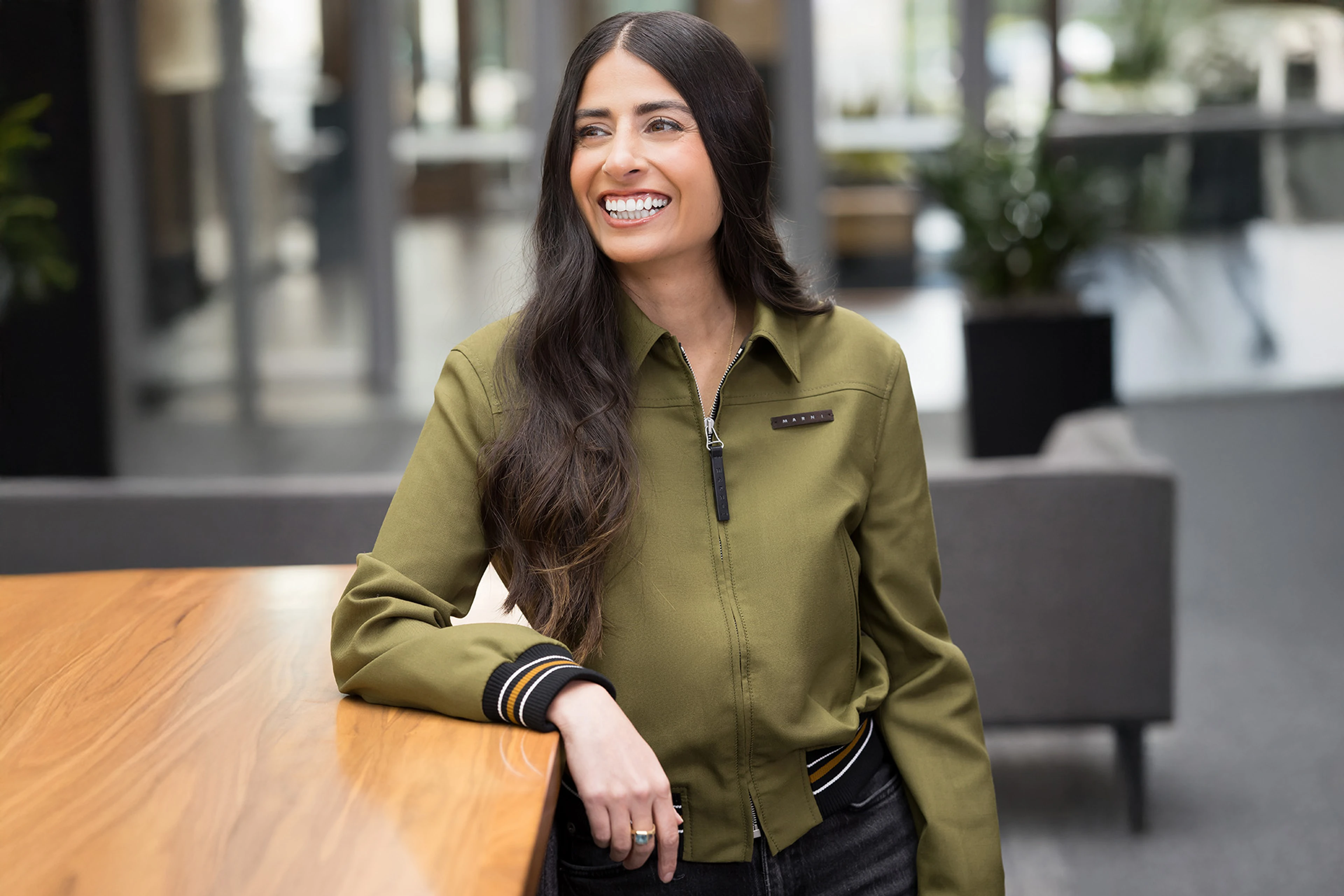 Xbox CEO Asha Sharma smiles while standing beside a wooden table in an office.