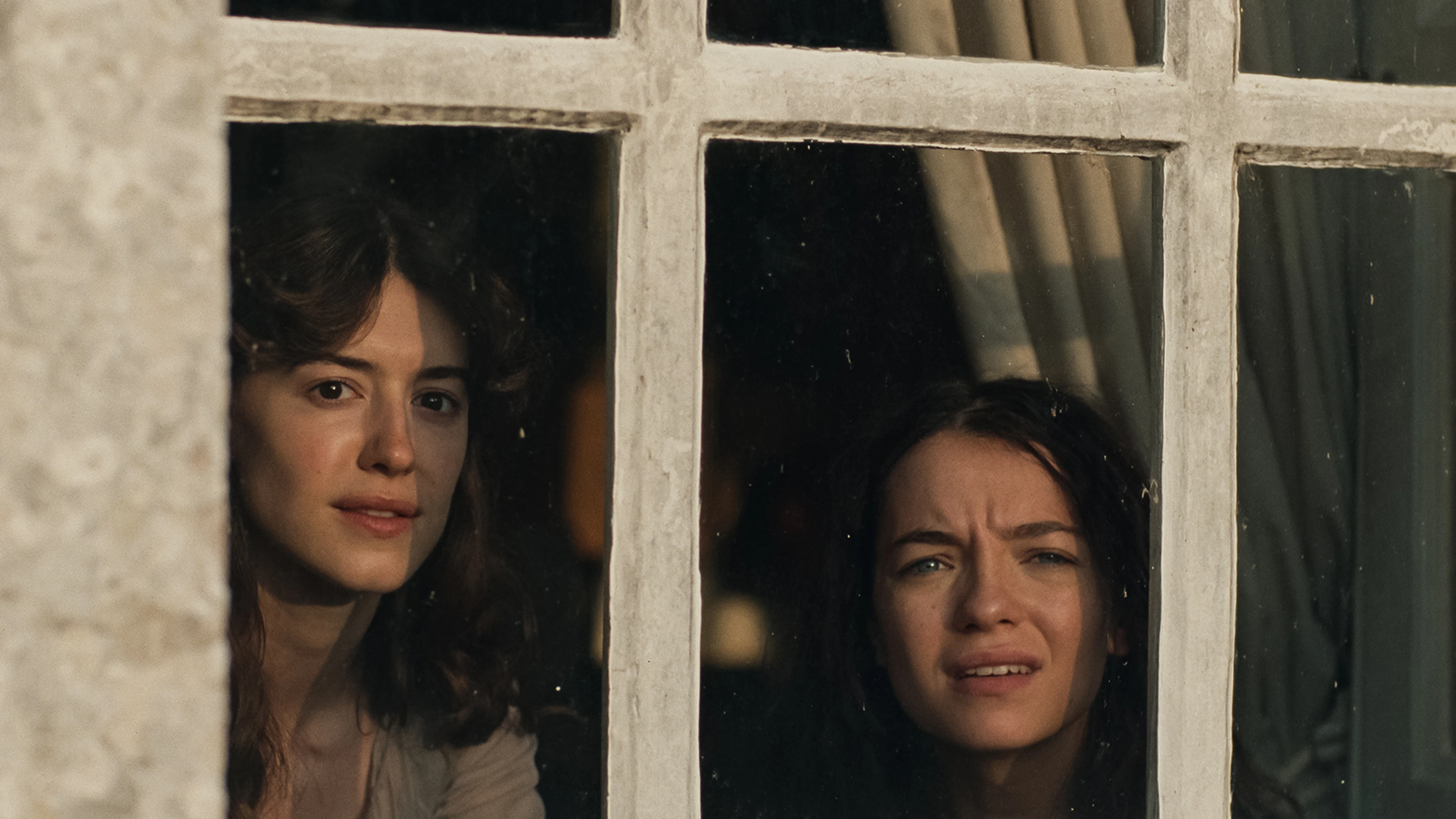 Elinor and Marianne Dashwood look out through the panes of a cottage window.