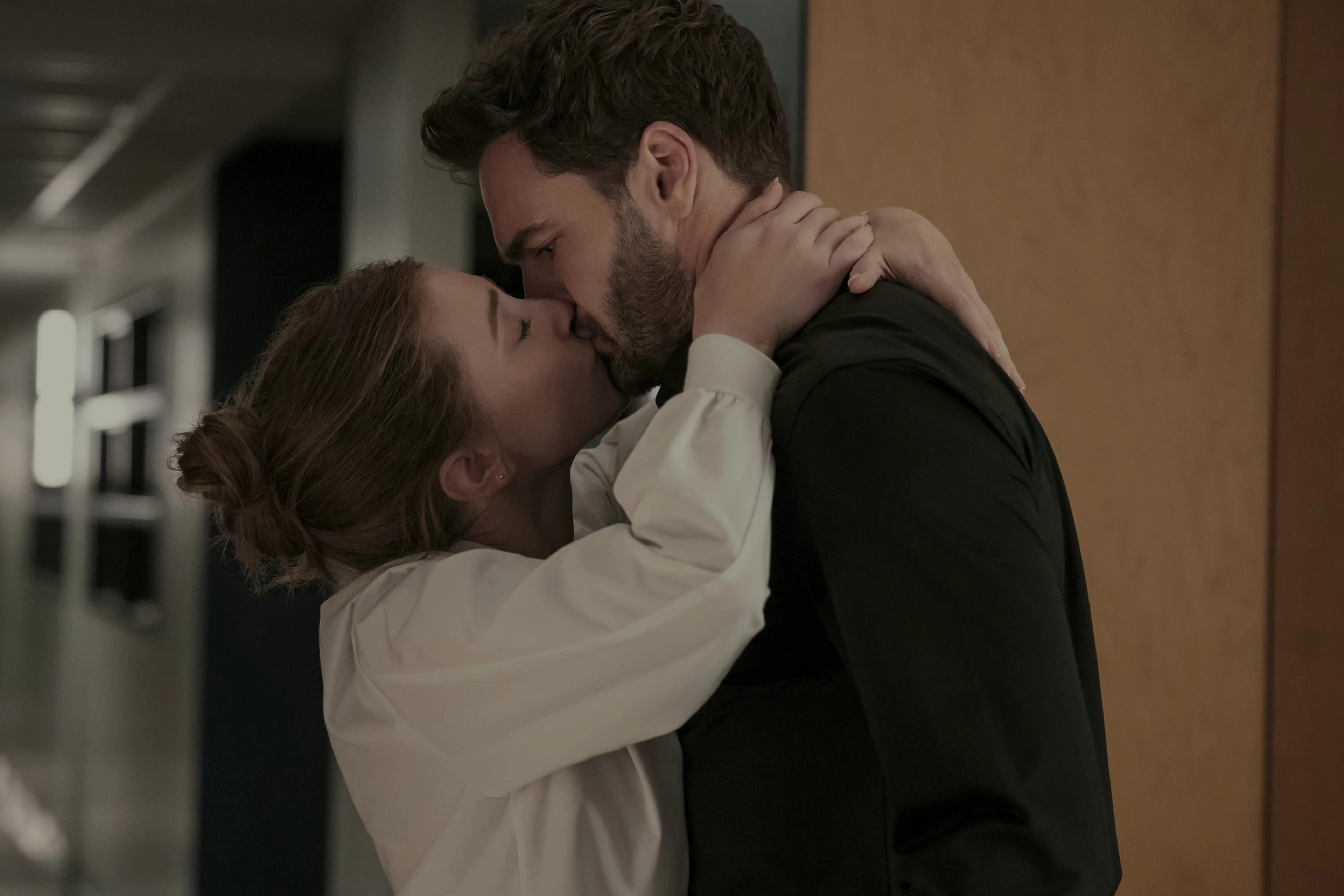 Olive and Adam kiss in a university corridor.