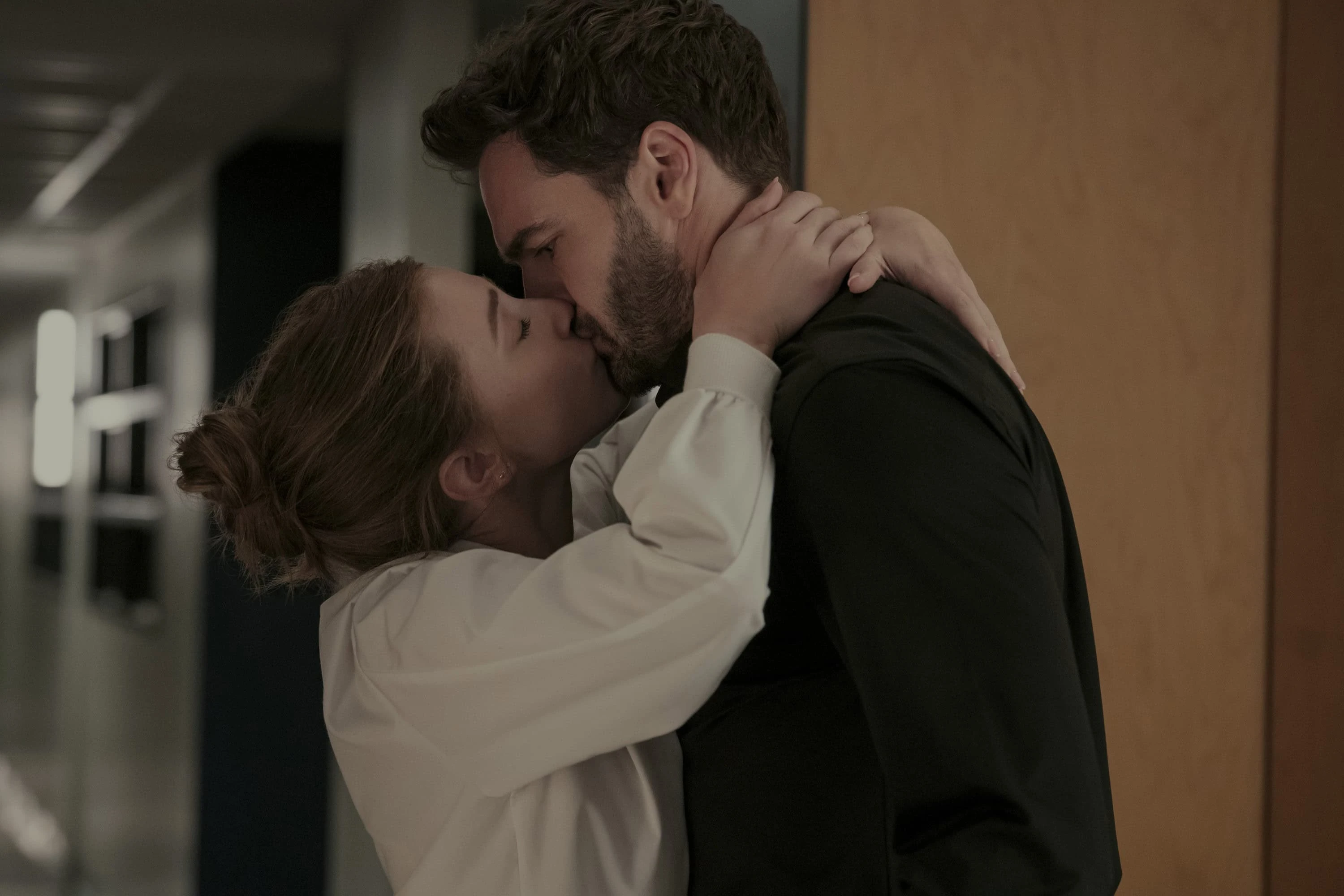 Olive and Adam kiss in a university corridor.