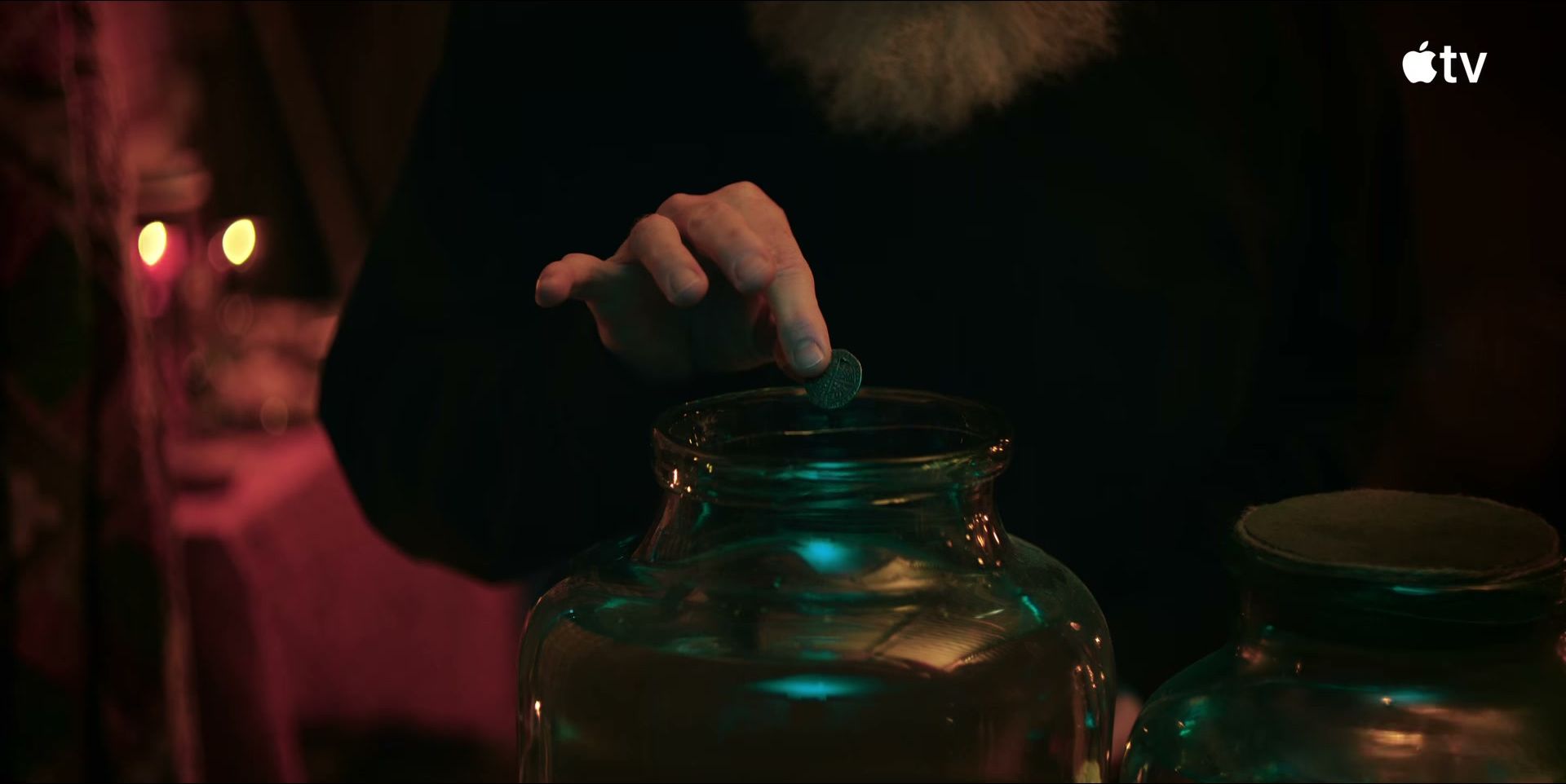 A hand lowers a small object into a large glass jar beside another jar.