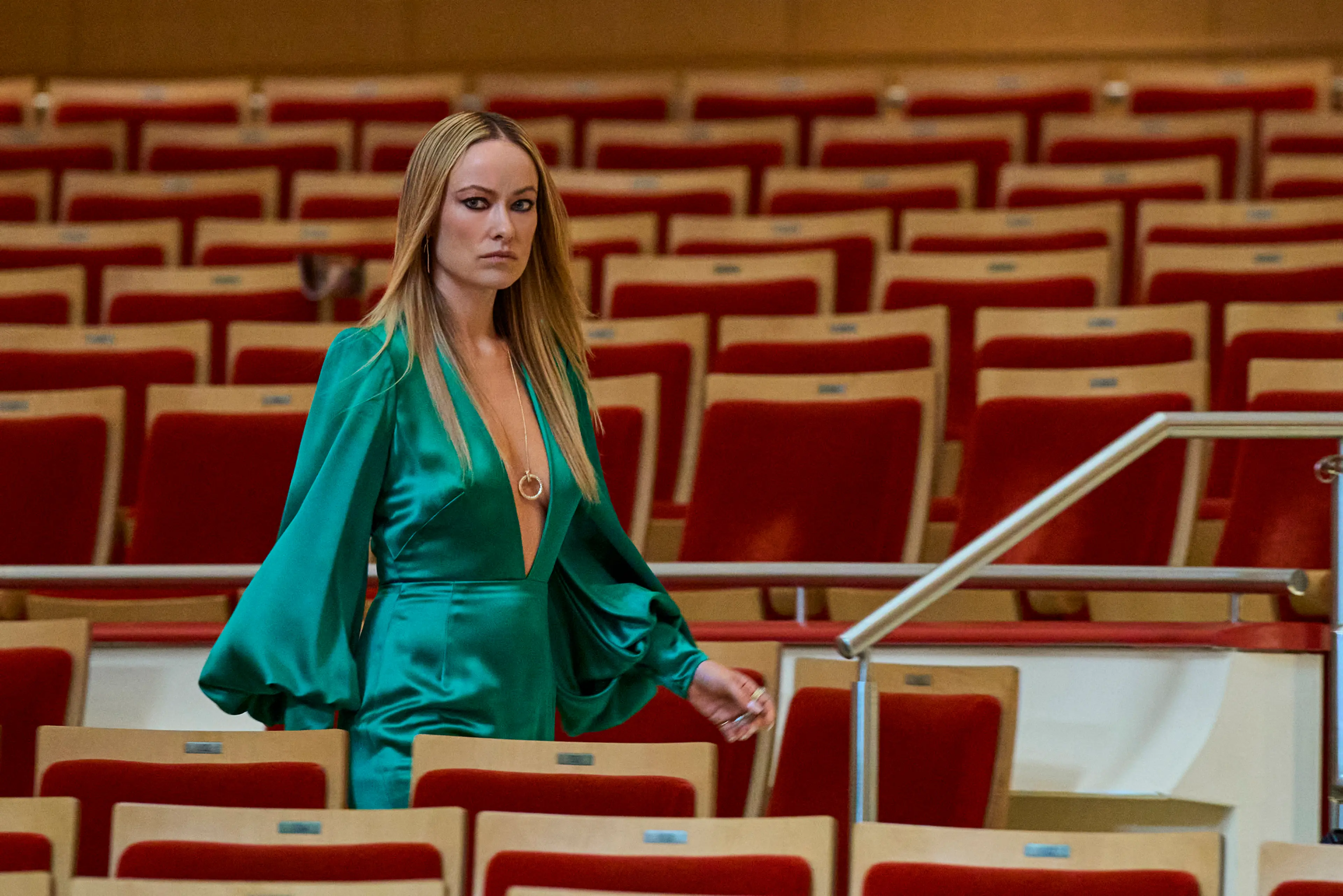 Olivia Wilde stands among rows of seats in a concert hall in Behemoth!.