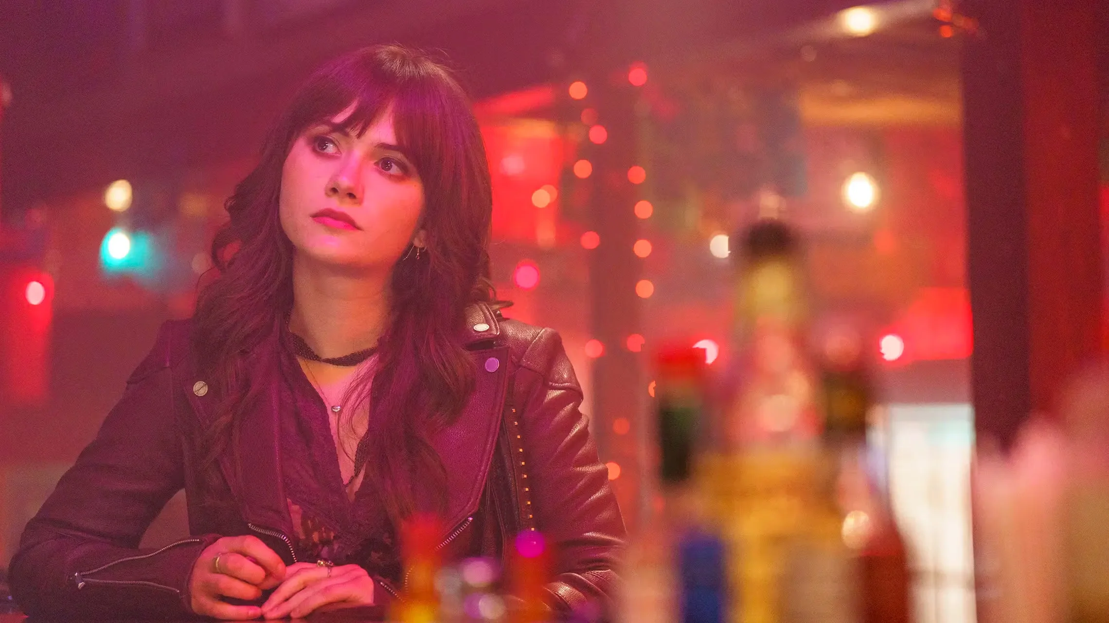 Harper sits alone at a table in a red-lit room.