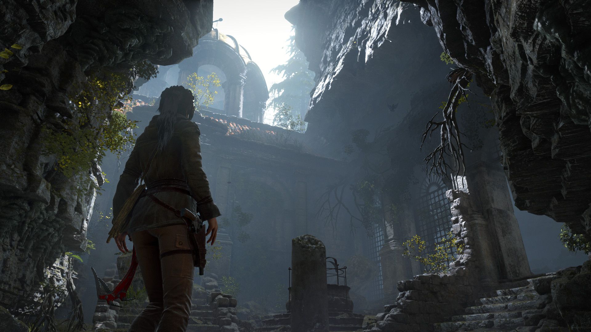 Lara stands inside a shadowy cave opening looking toward a brighter mountain route.