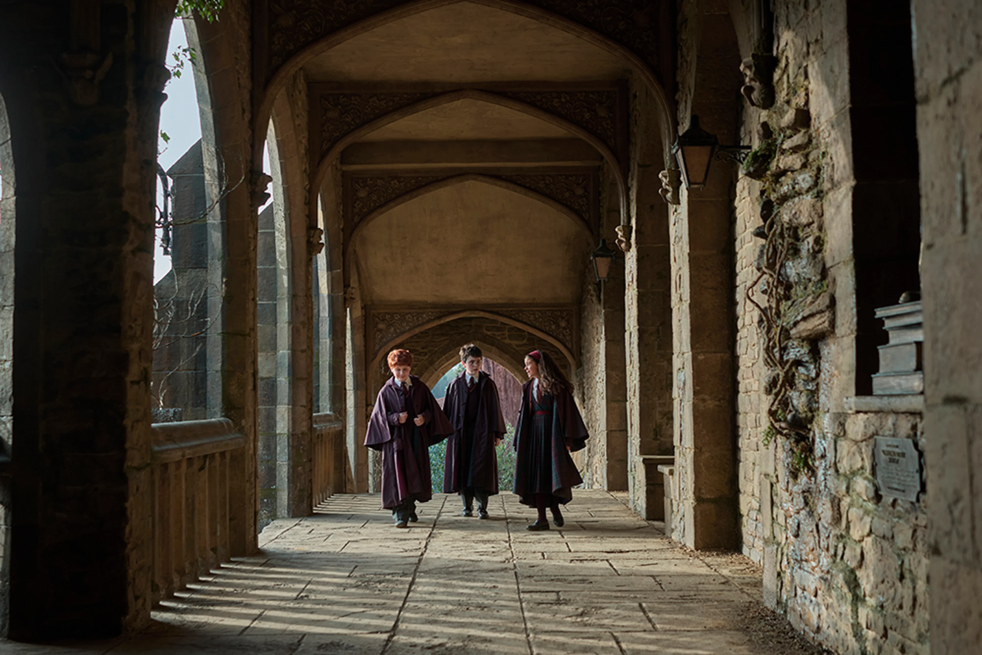 The new Harry Potter, Ron Weasley, and Hermione Granger walk through Hogwarts in an official teaser still.