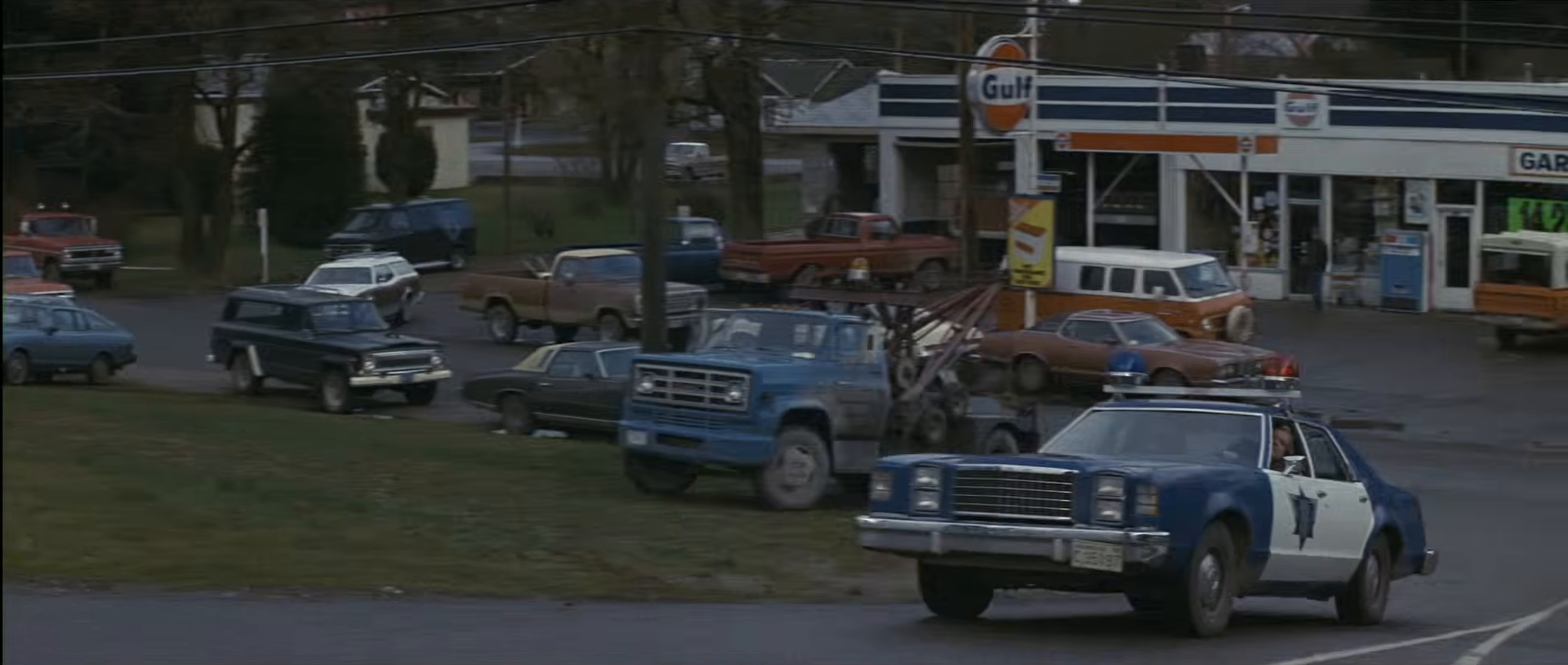 Several police vehicles pass a small-town gas station in First Blood.