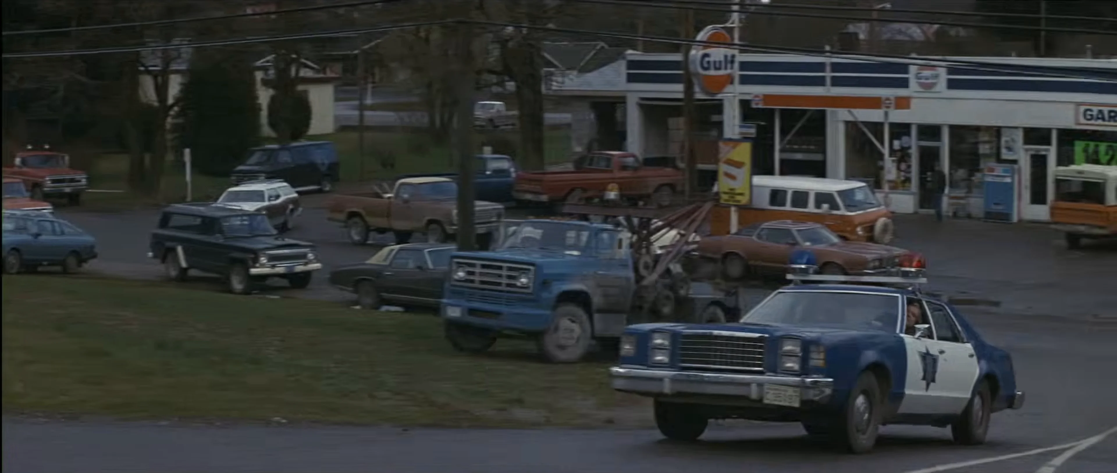 Several police vehicles pass a small-town gas station in First Blood.