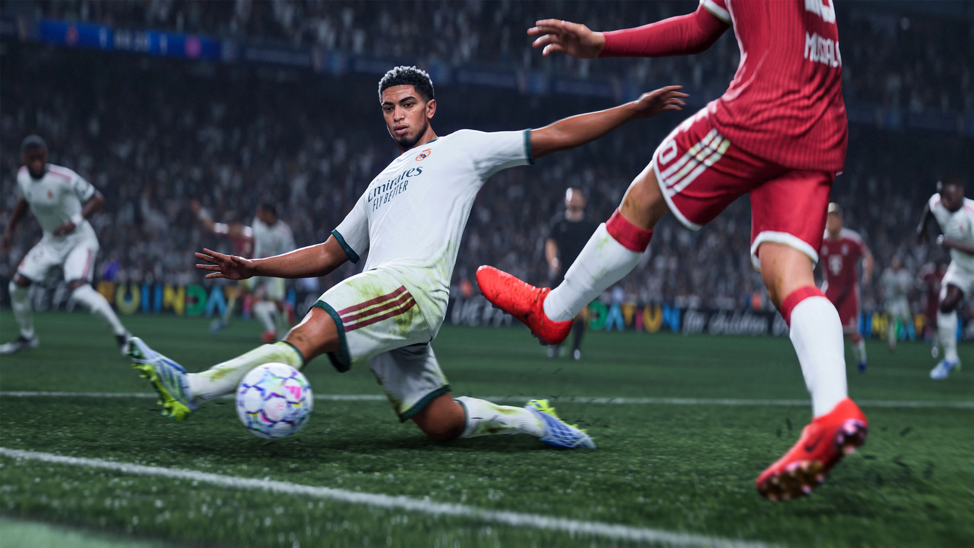 Jude Bellingham slides toward the ball as a Bayern player in red tries to reach it.