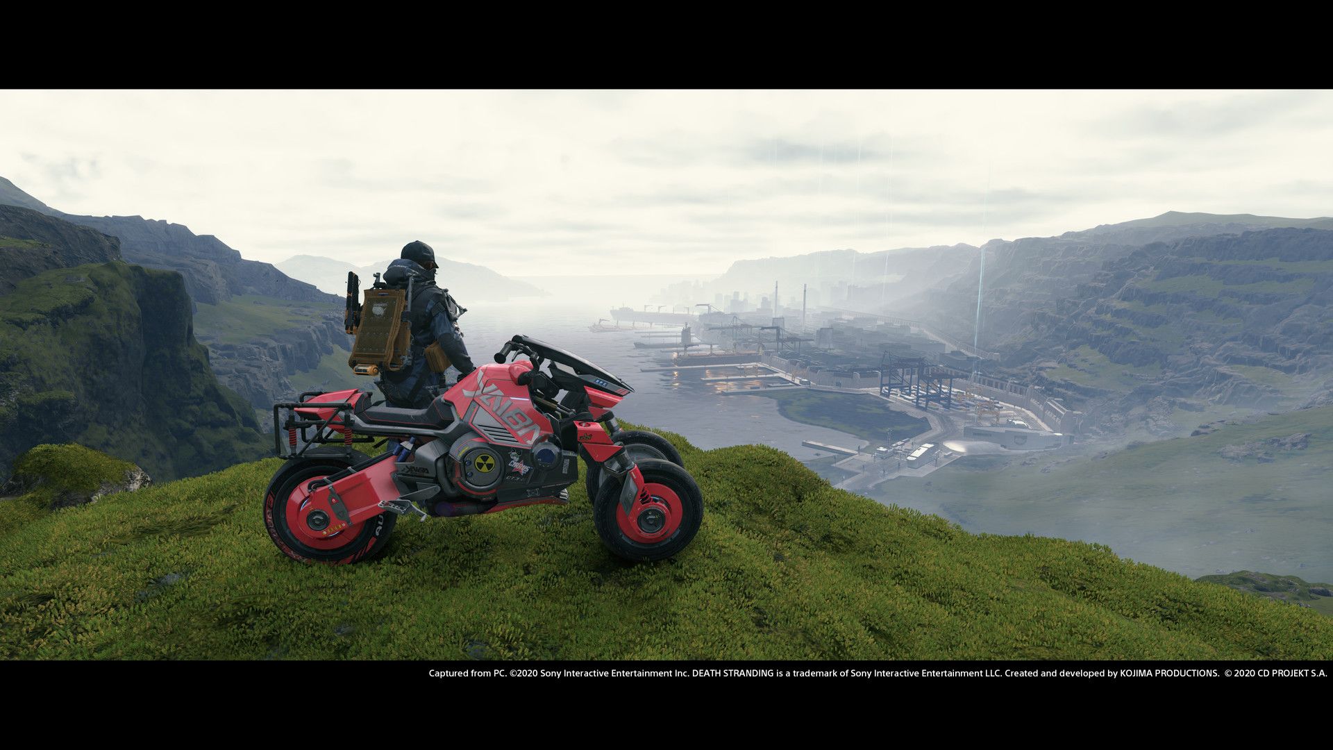 Sam stands beside a motorbike overlooking the open landscape.