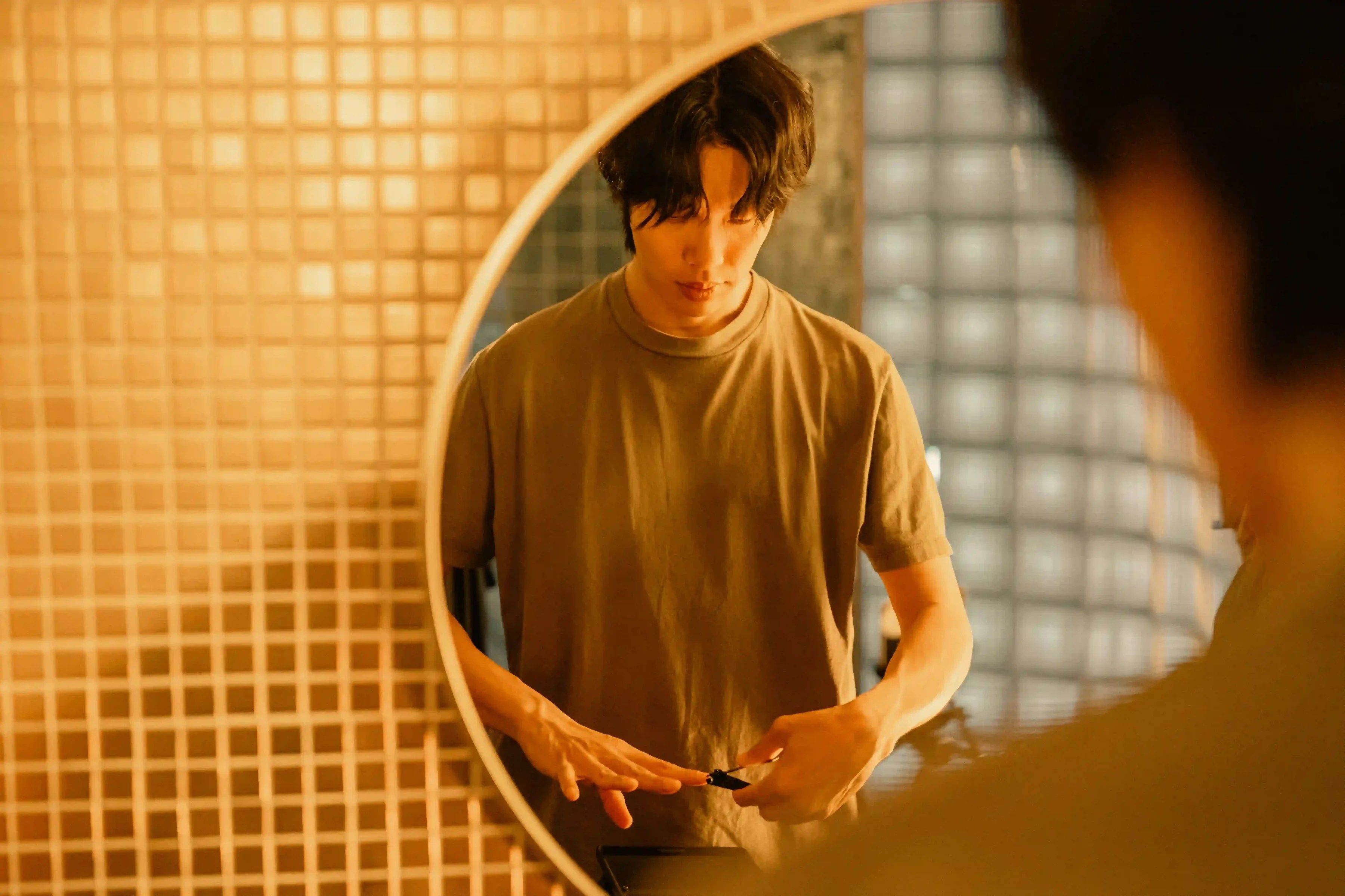 Moon-jae looks into a round bathroom mirror with his hands held near his waist.