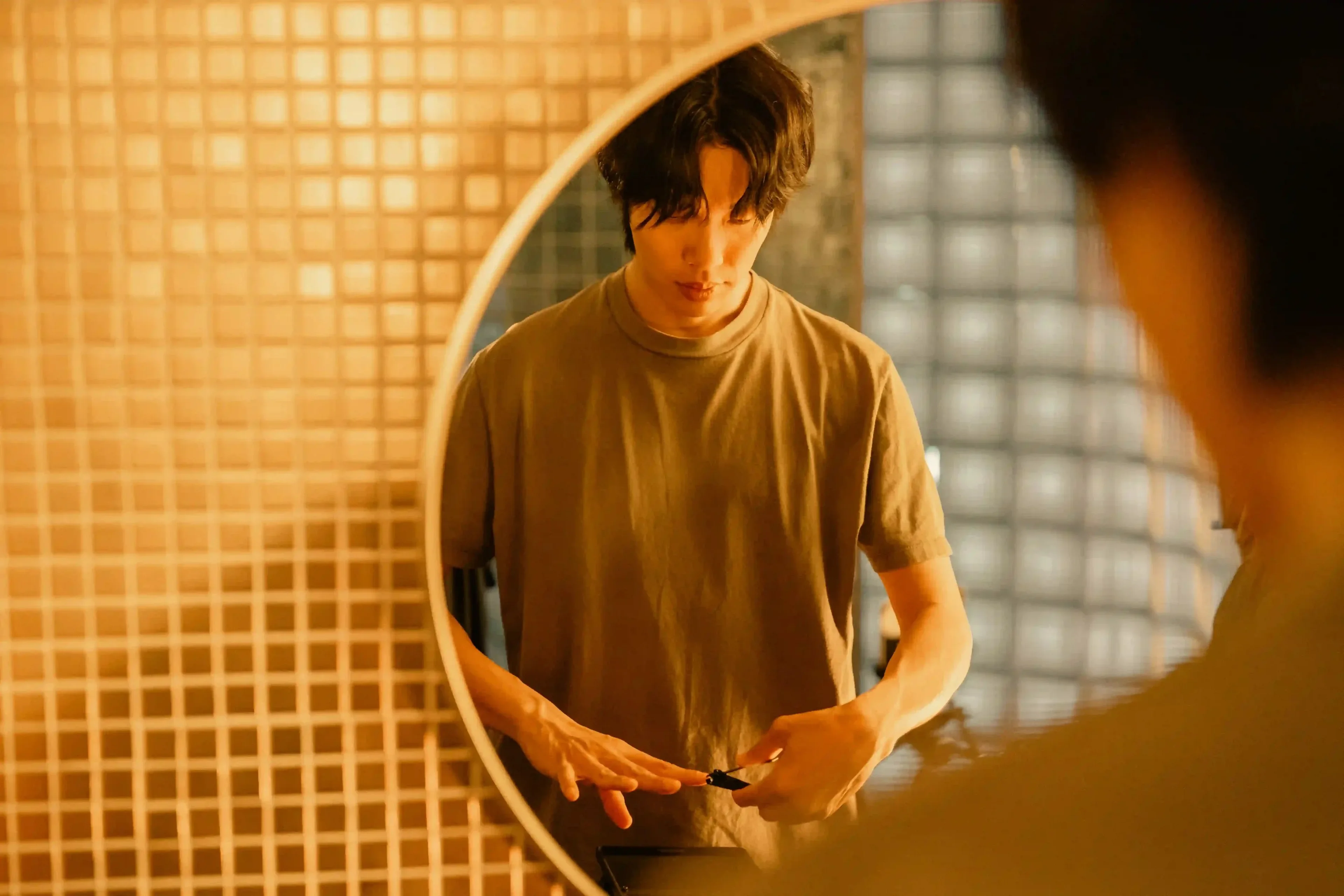 Moon-jae looks into a round bathroom mirror with his hands held near his waist.