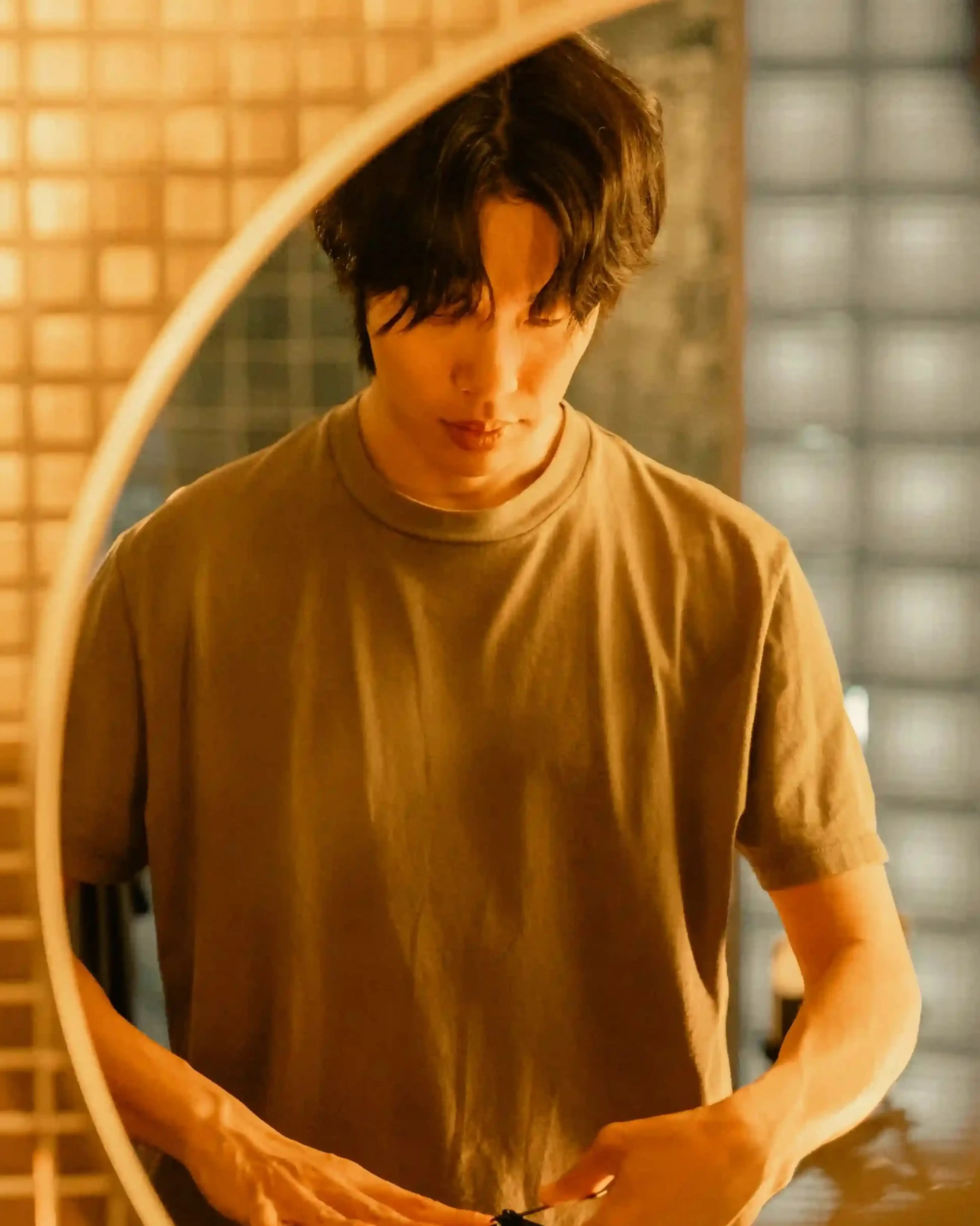 Moon-jae looks into a round bathroom mirror with his hands held near his waist.