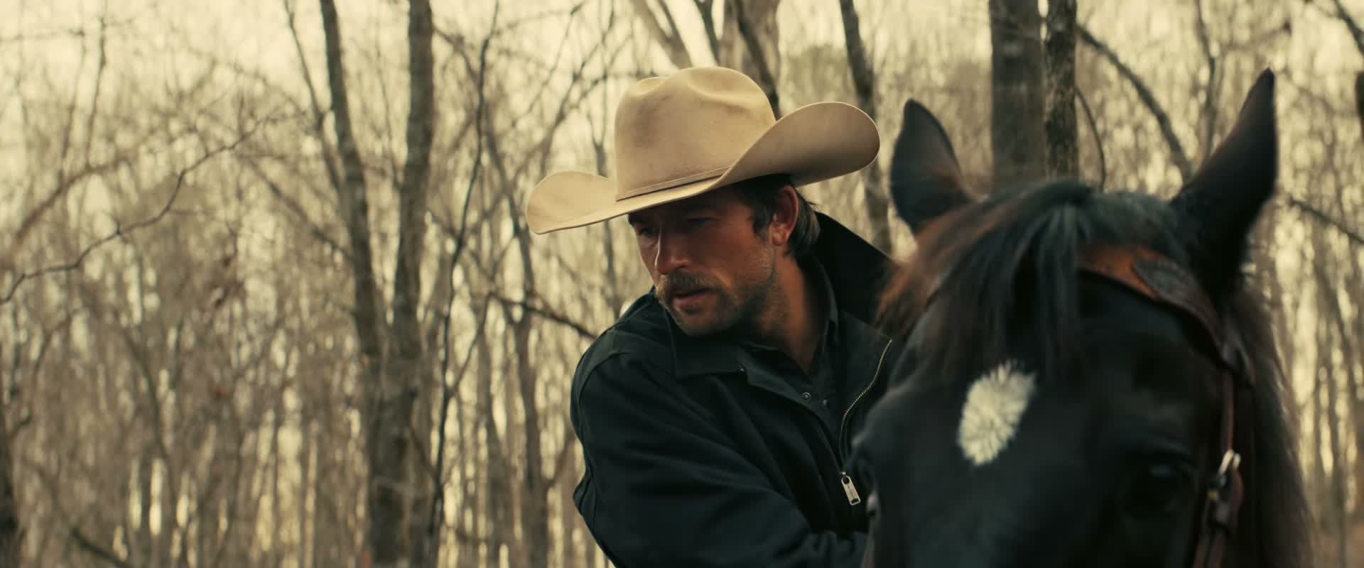 The cowboy rides through the woods on horseback.