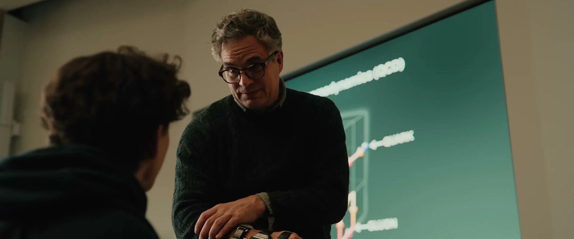Mark Ruffalo as Bruce Banner speaks to Peter in a classroom while touching a device on his wrist.