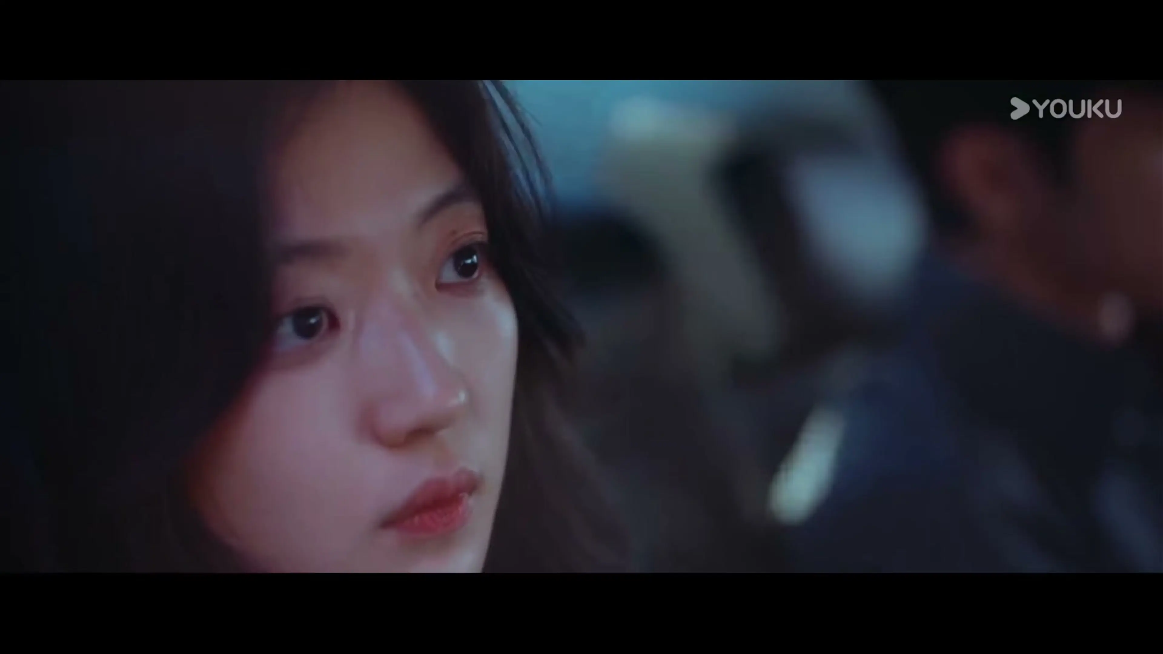 Sun Qian looks toward a man in a close-up, with her hair tucked behind one ear.