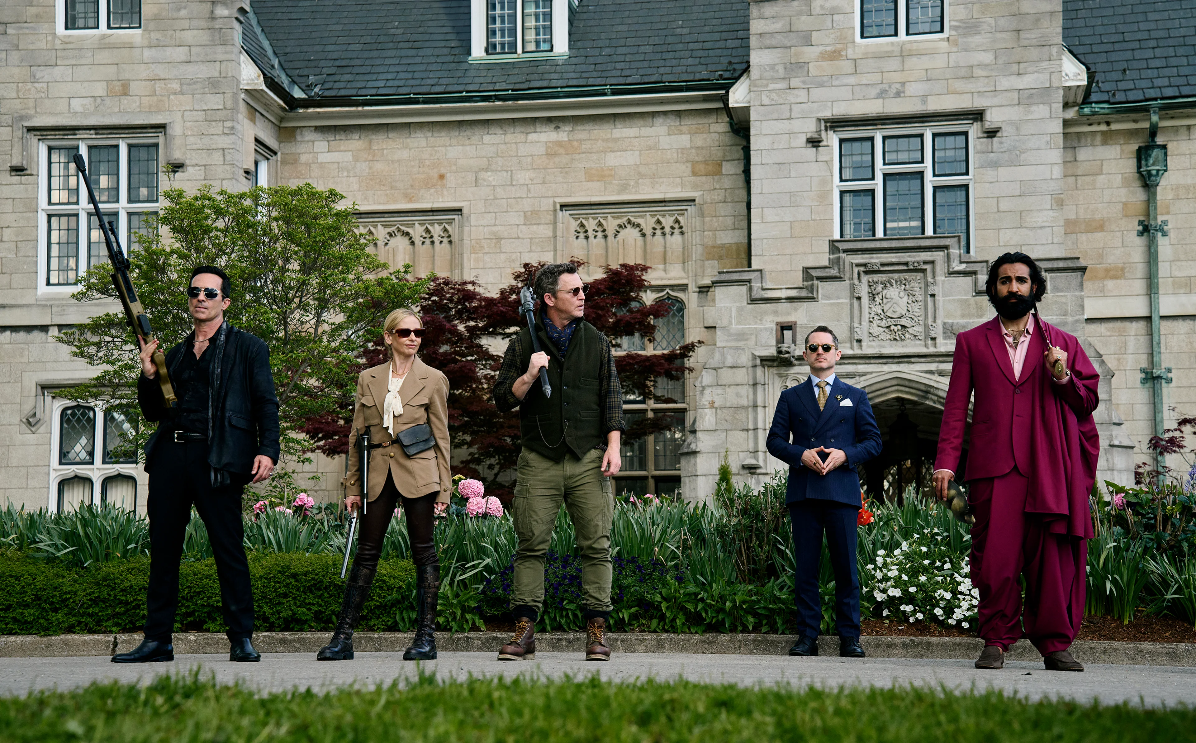 The armed hunters and the Lawyer stand outside a large stone building.