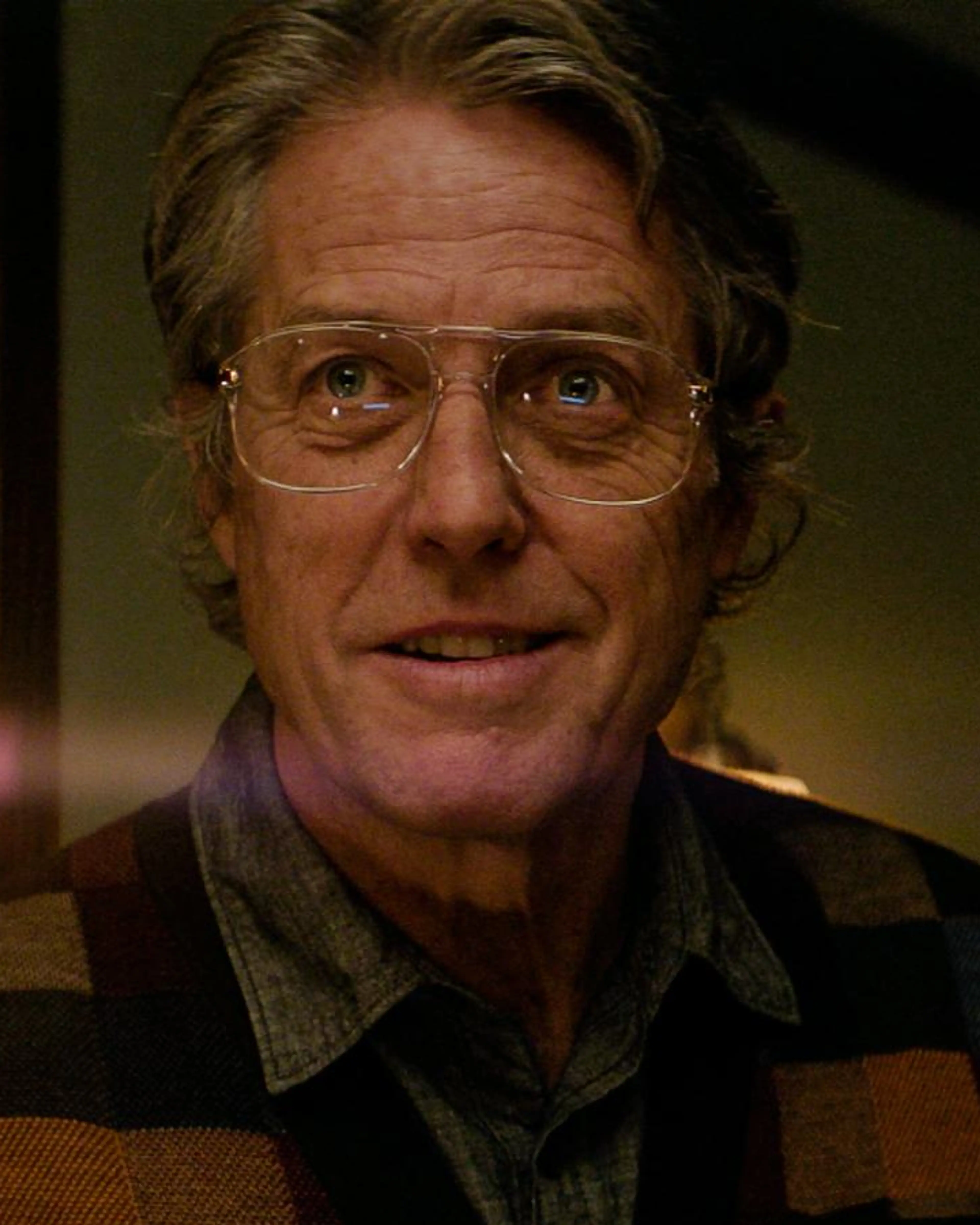 Hugh Grant as Mr. Reed holds a lit candle while wearing glasses and a checked cardigan.