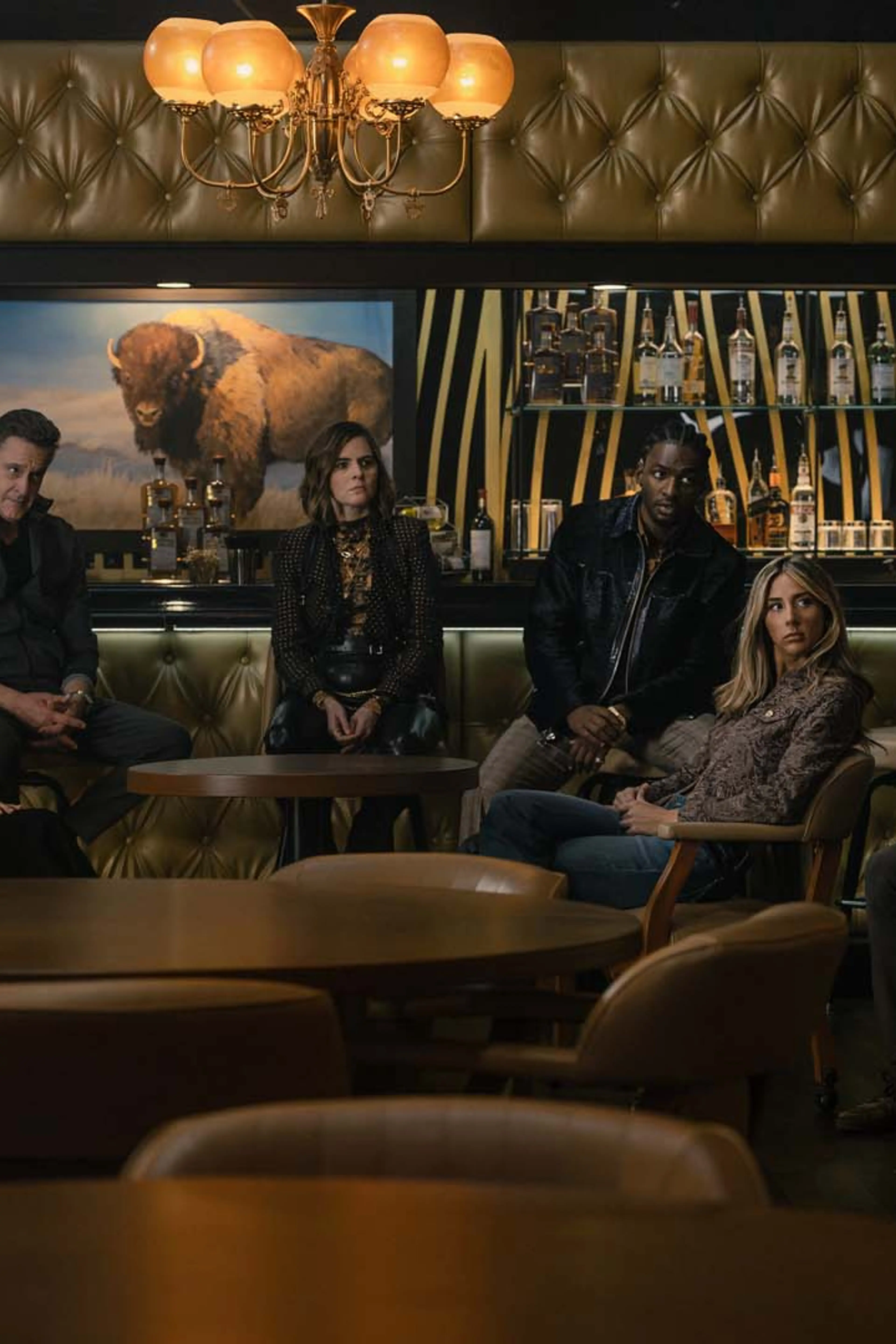 Garrett Hedlund, Annabella Sciorra, Chris Caldovino, McKenna Quigley Harrington, Jay Will, Scarlet Stallone, and Martin Starr gather in a bar in Tulsa King Season 4.