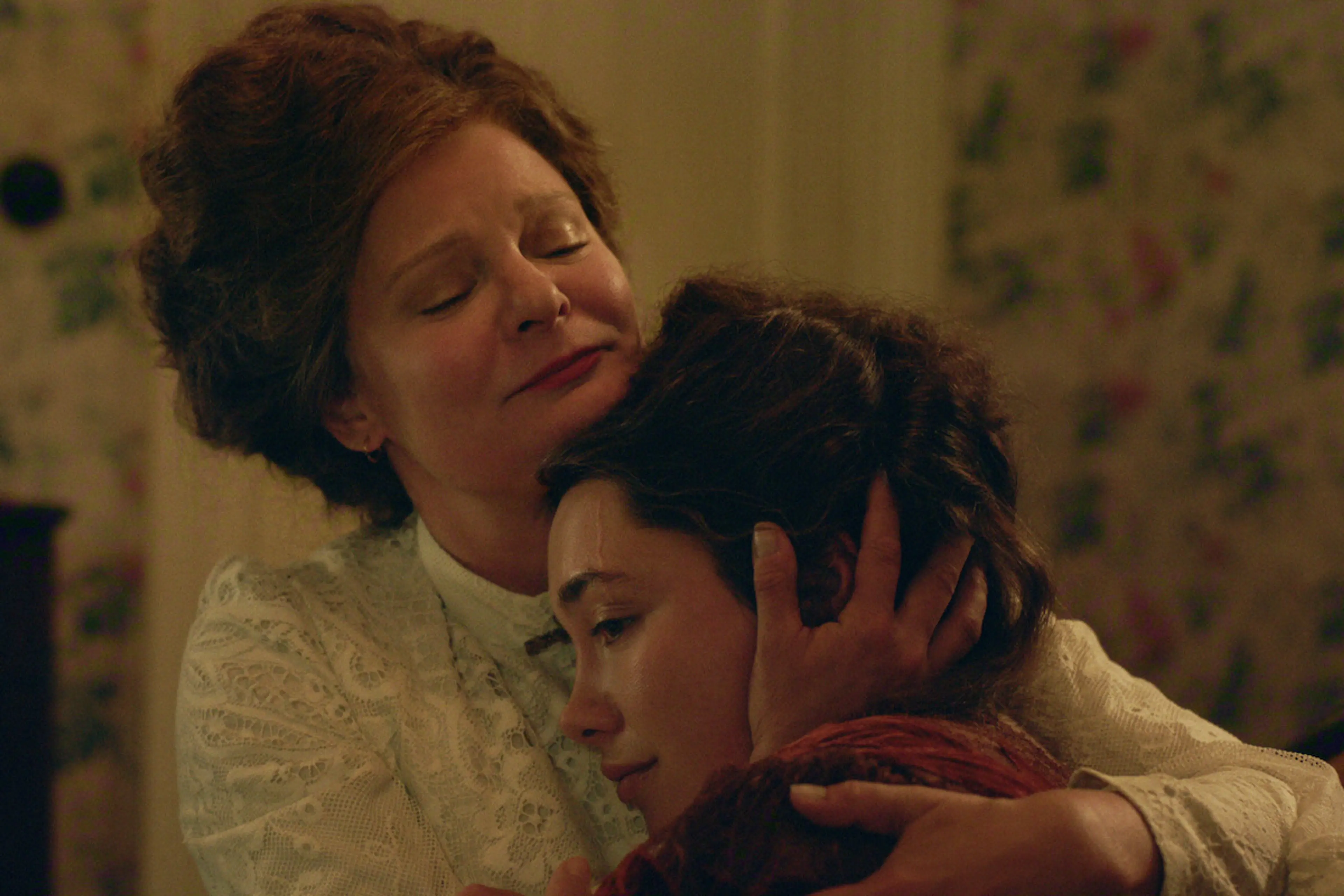 Two women in period clothing share an emotional embrace in a floral room in East of Eden.