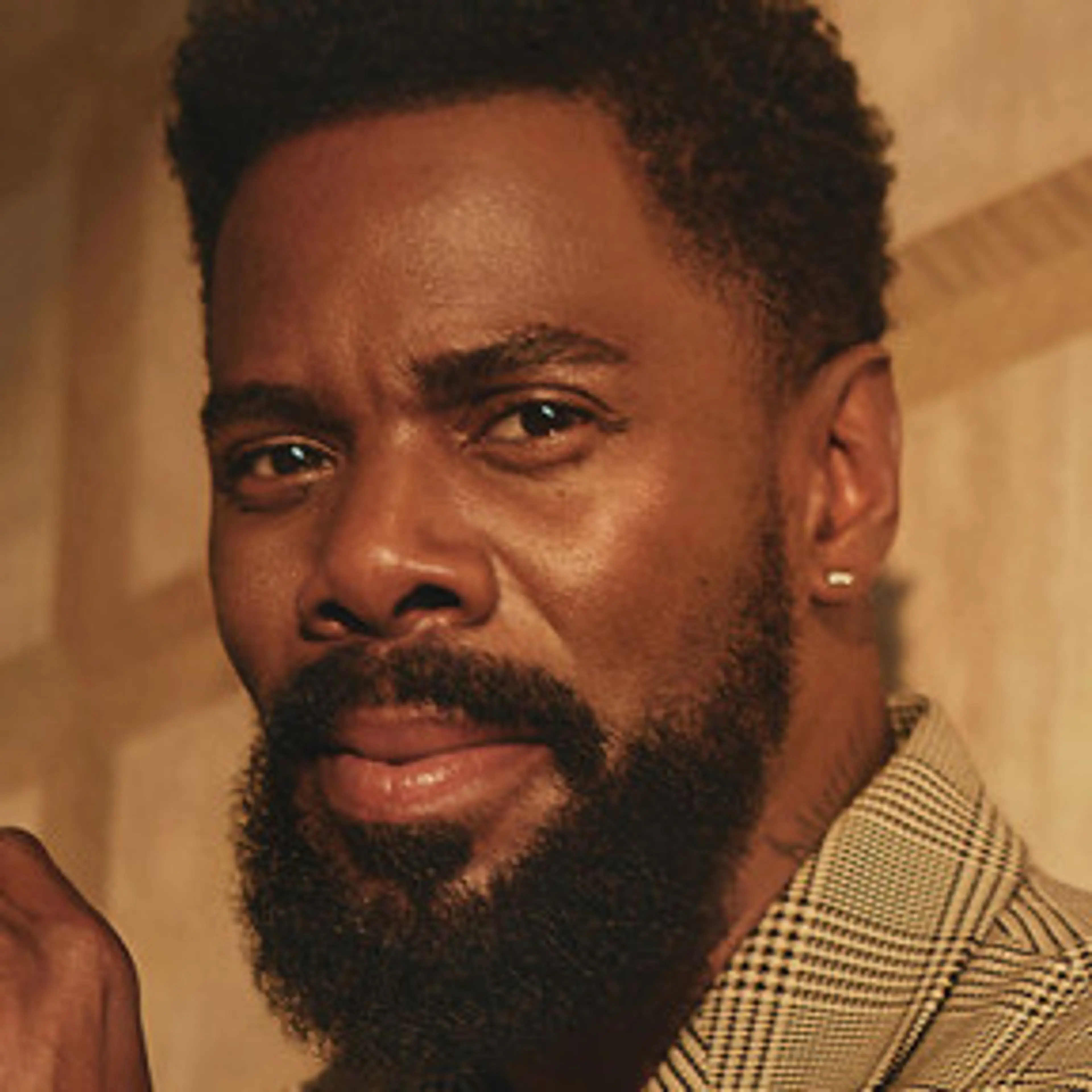 Portrait of Colman Domingo with a beard and checked jacket in warm light.
