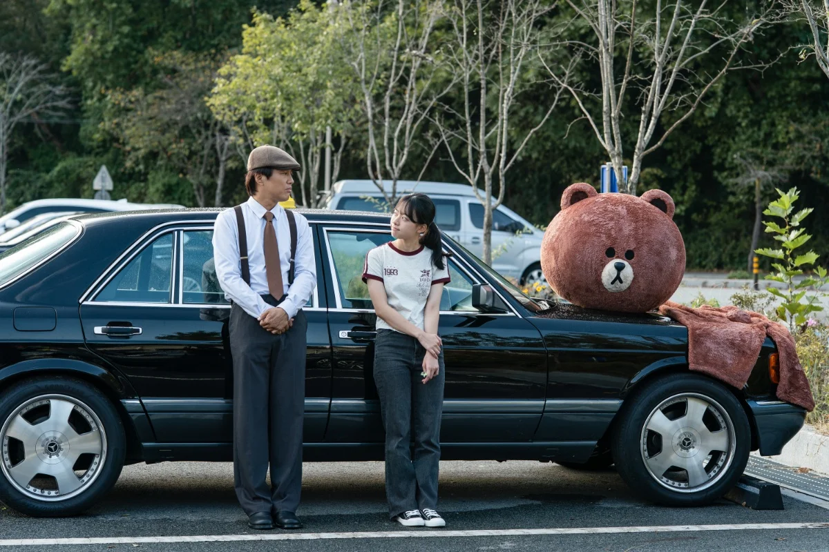 Cha Tae-hyun and Lee Jae-in stand beside a classic taxi with a large toy bear in Your Personal Taxi.