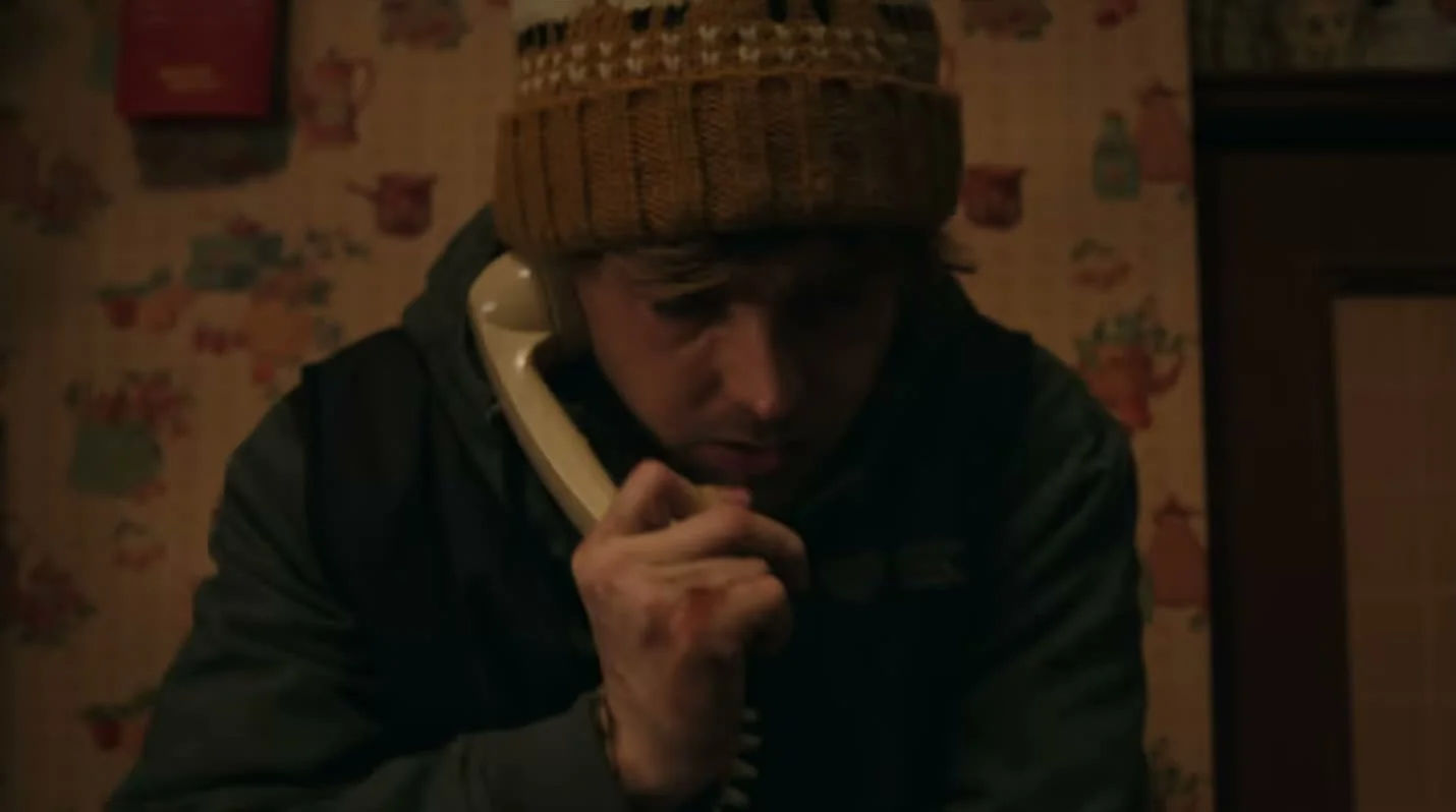 Bryan, wearing a knitted cap, grips a telephone in a tense scene from Resident Evil.