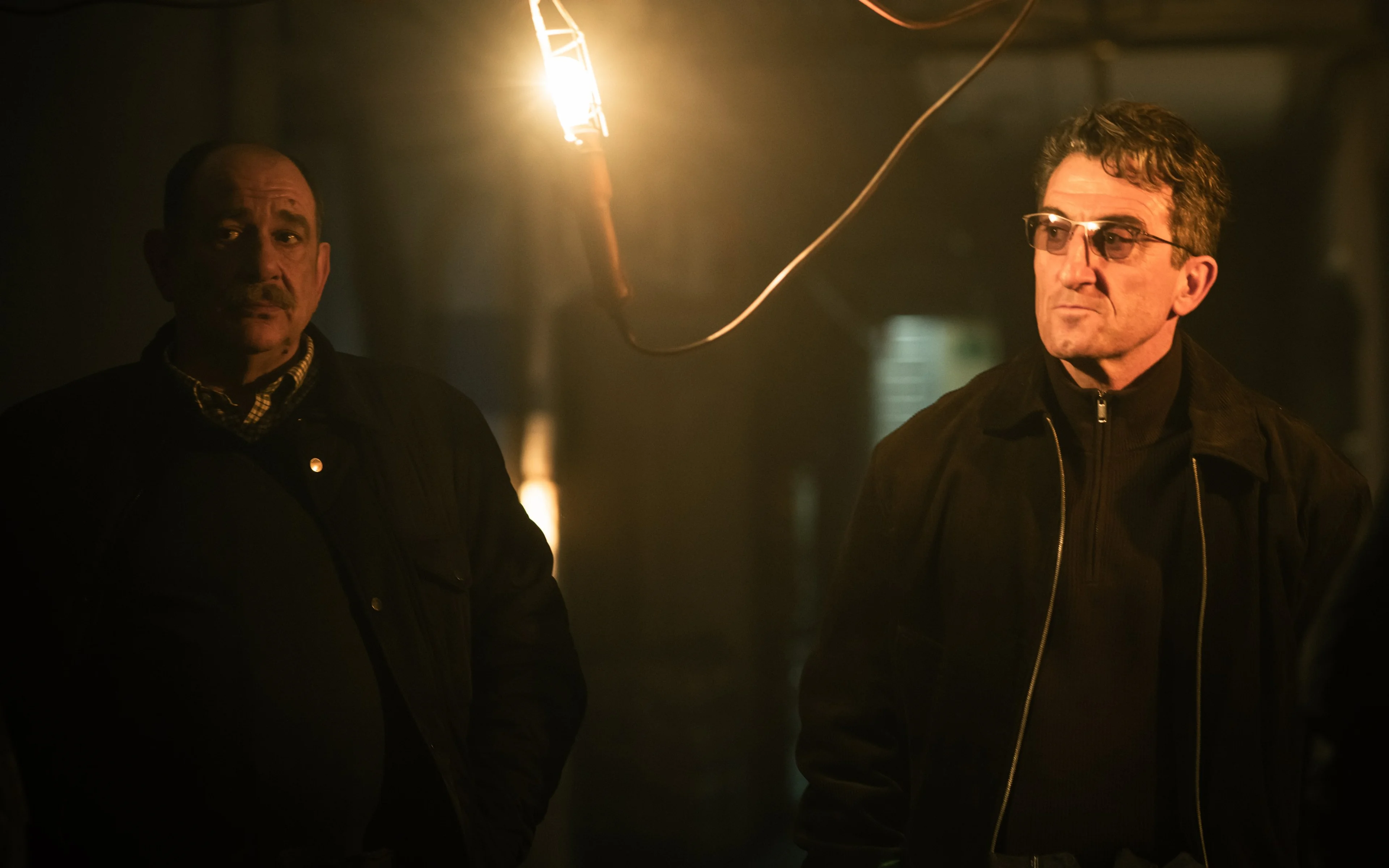 Two men face each other in a dim room.