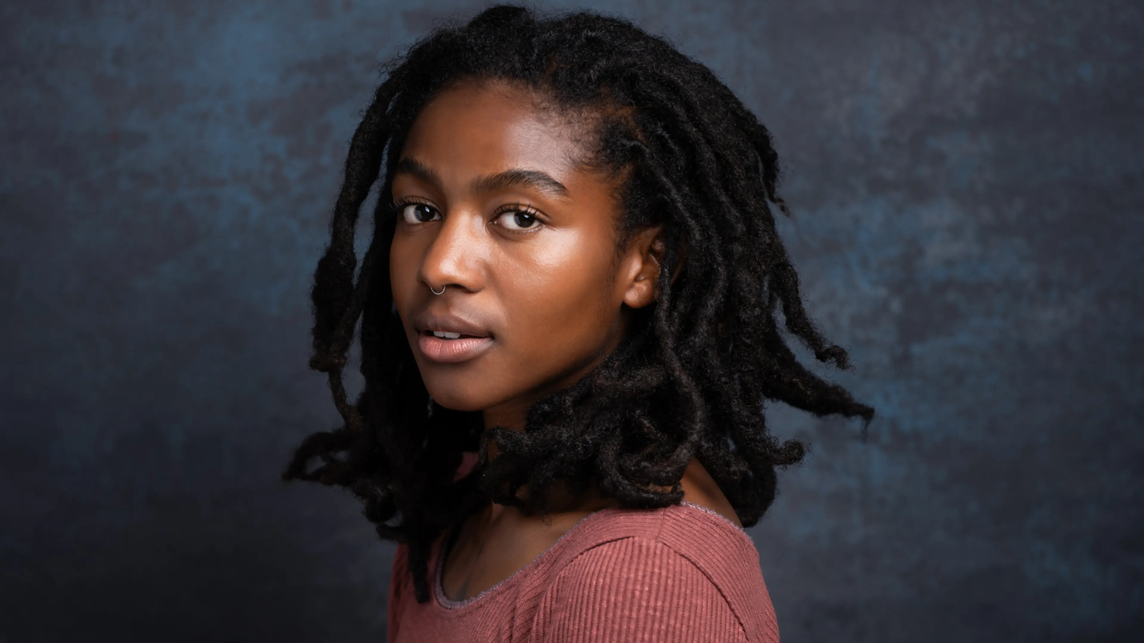 A close-up portrait of actor Adia against a blue-gray background.