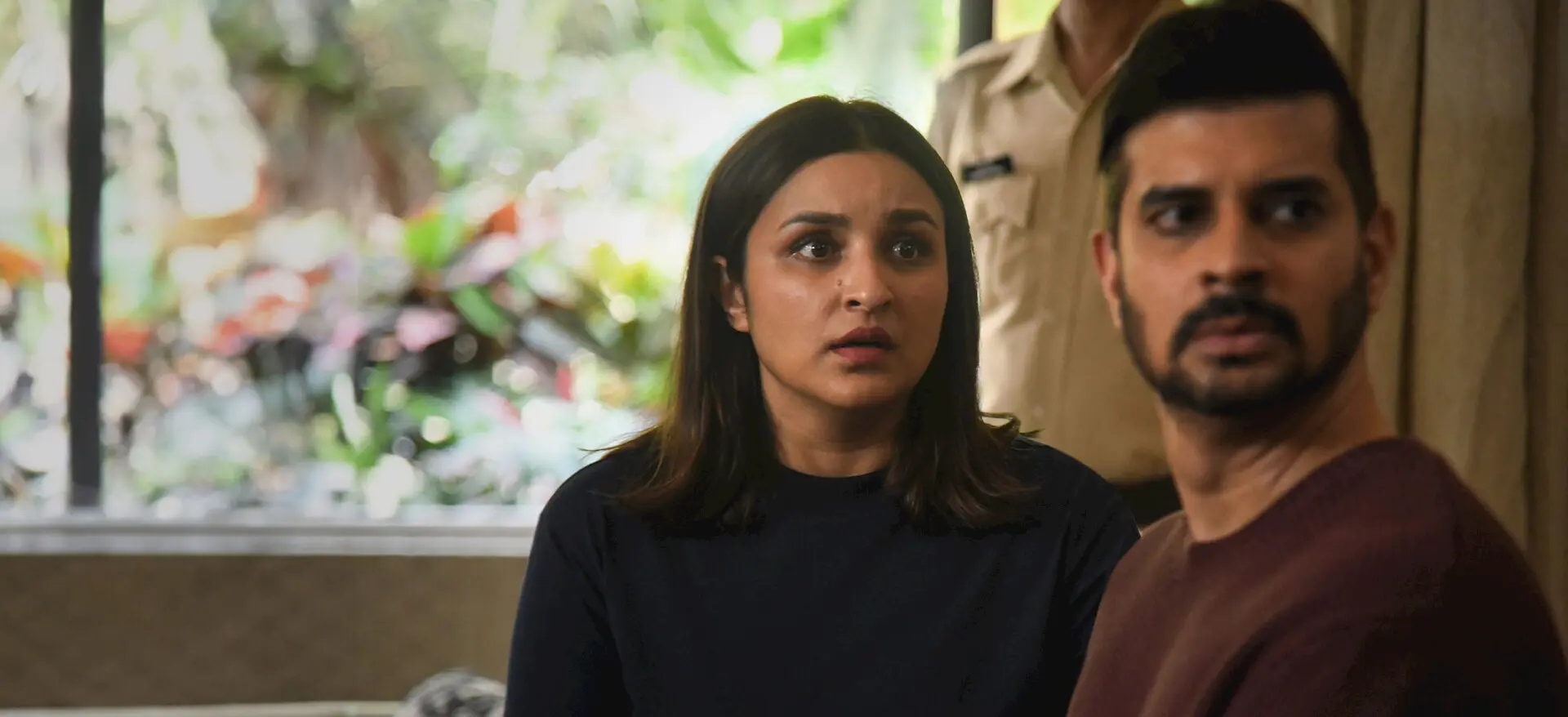 Parineeti Chopra and Tahir Raj Bhasin sit beside each other while a police officer stands behind them.