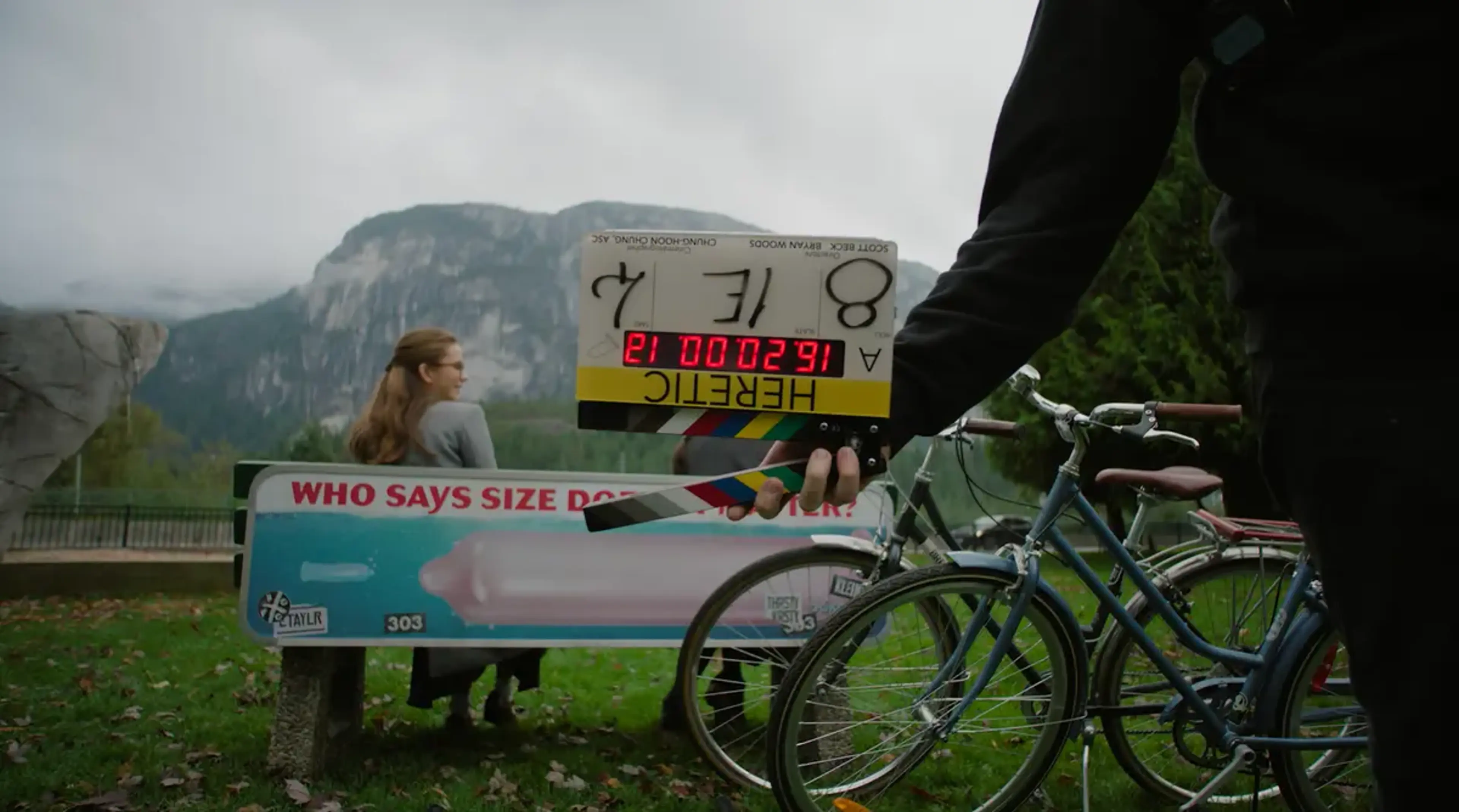 A film clapperboard is held in front of an outdoor Heretic scene with a bicycle.