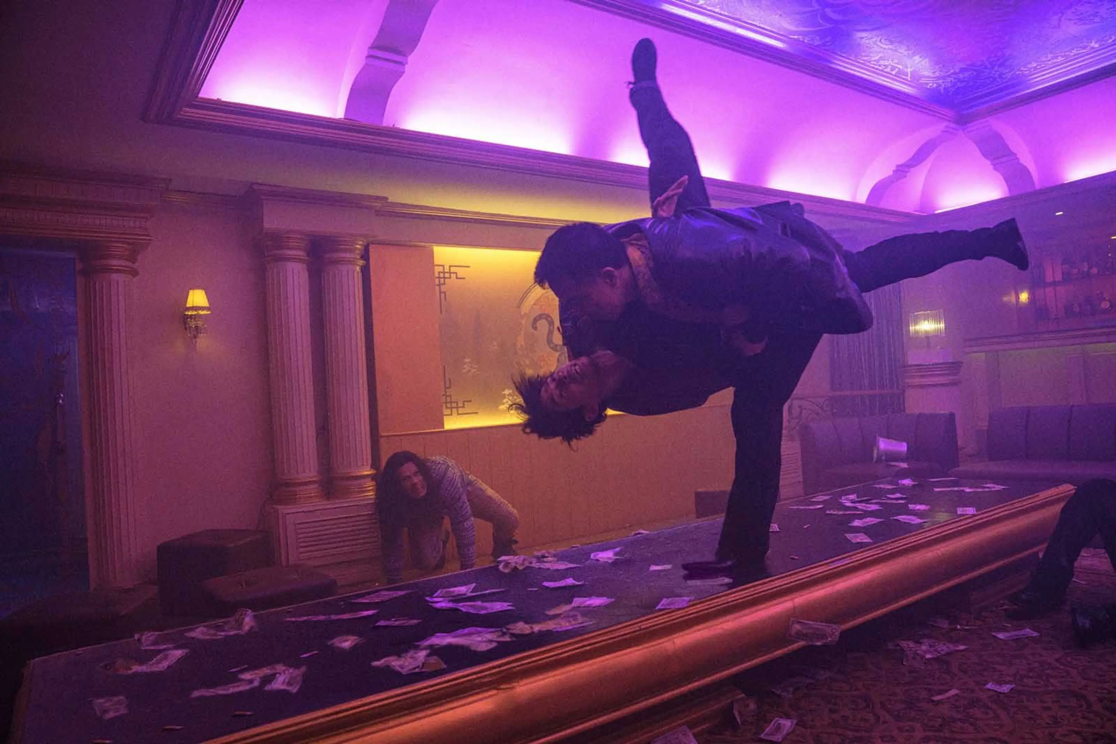 Two fighters grapple above a table in a room lit with purple light.
