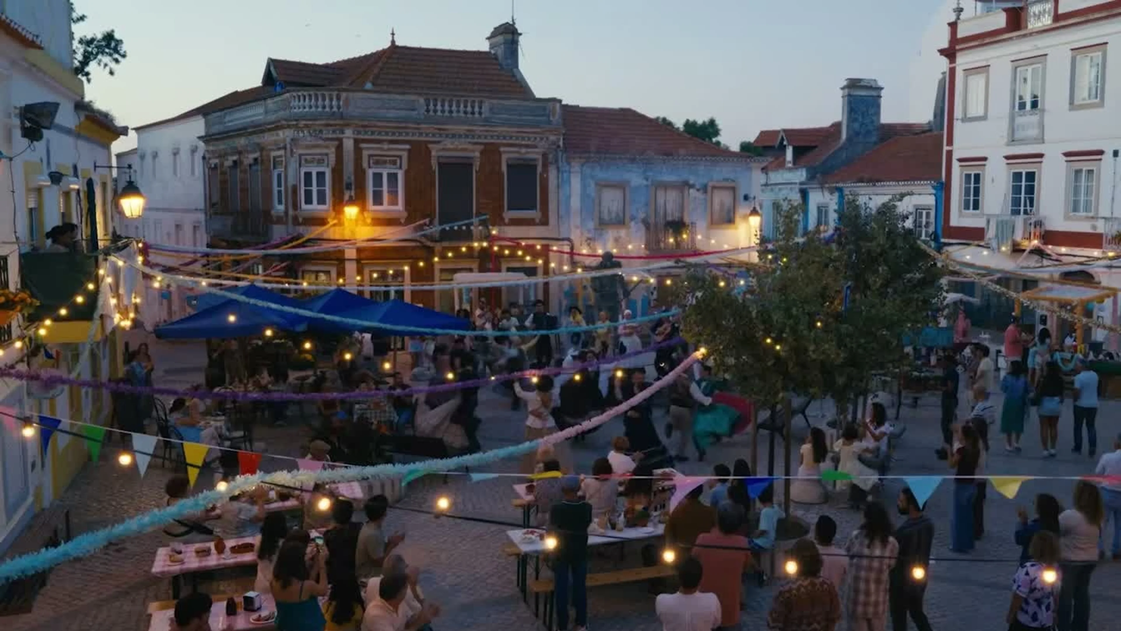 People gather under lights and streamers in a European town square in Love of Your Life.