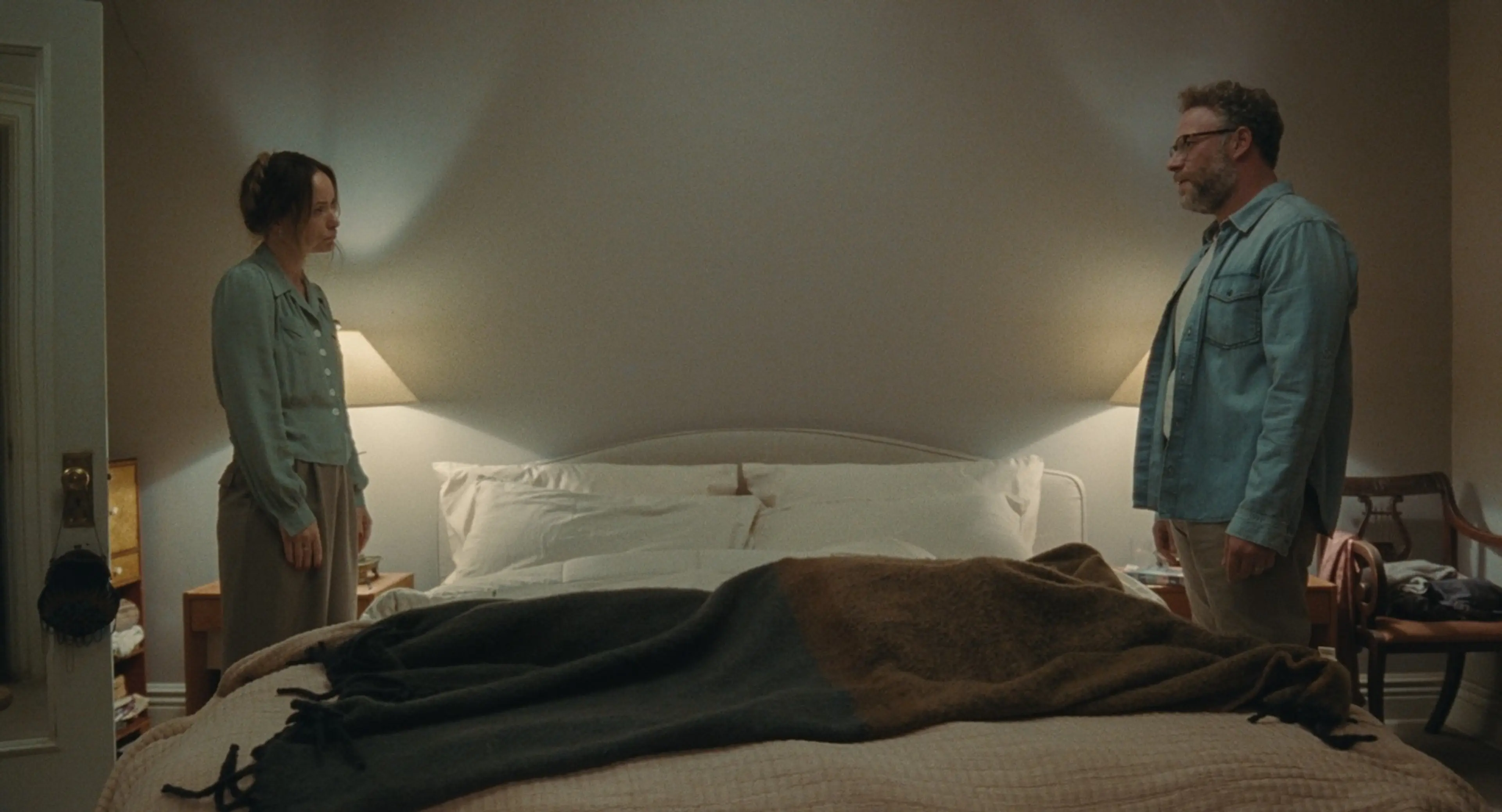 Angela and Joe stand on opposite sides of a bed.