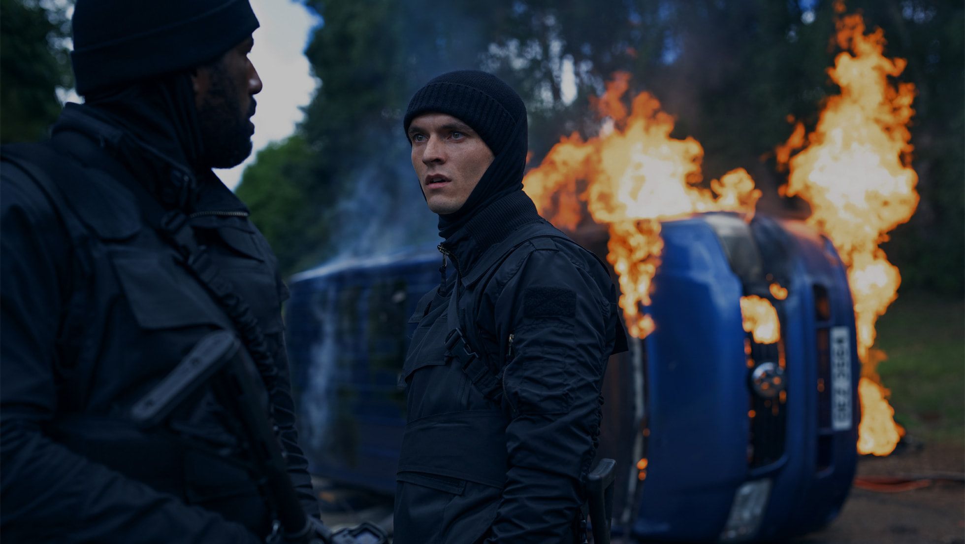 Gershwyn Eustache Jnr and Fionn Whitehead beside a burning car in The Wanted Man.