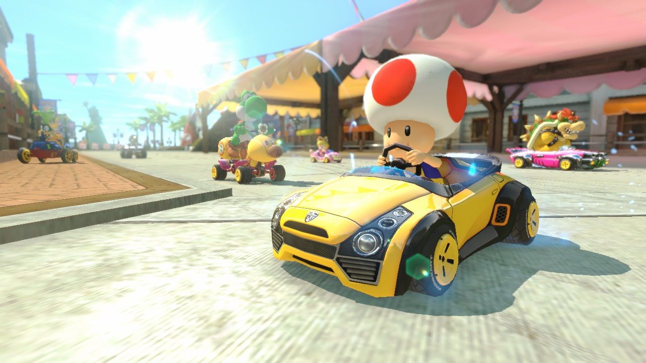 Toad drives a yellow kart along a bright street lined with storefronts.
