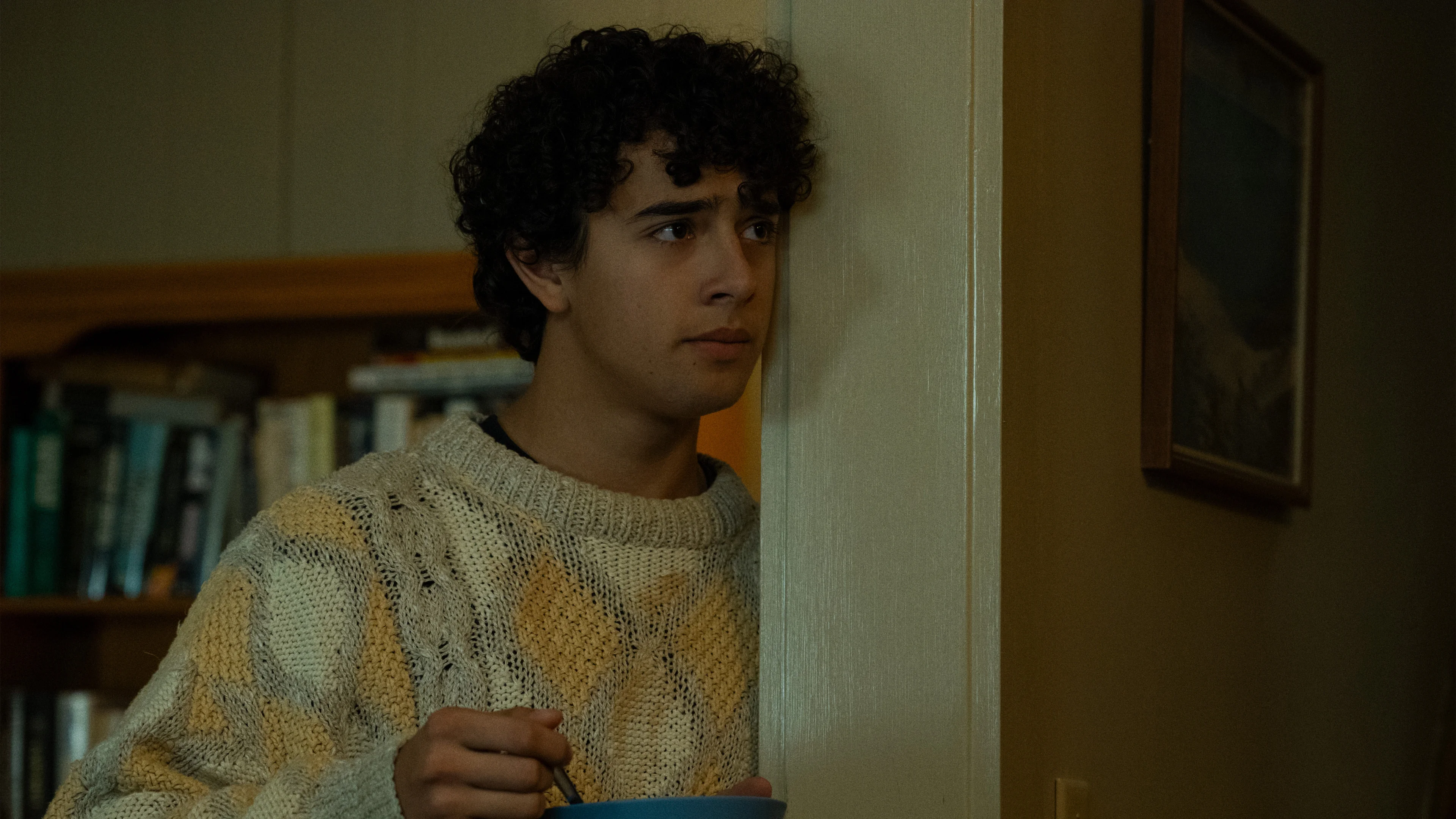 Kingston Rumi Southwick as Evan stands in a doorway, holding a bowl.