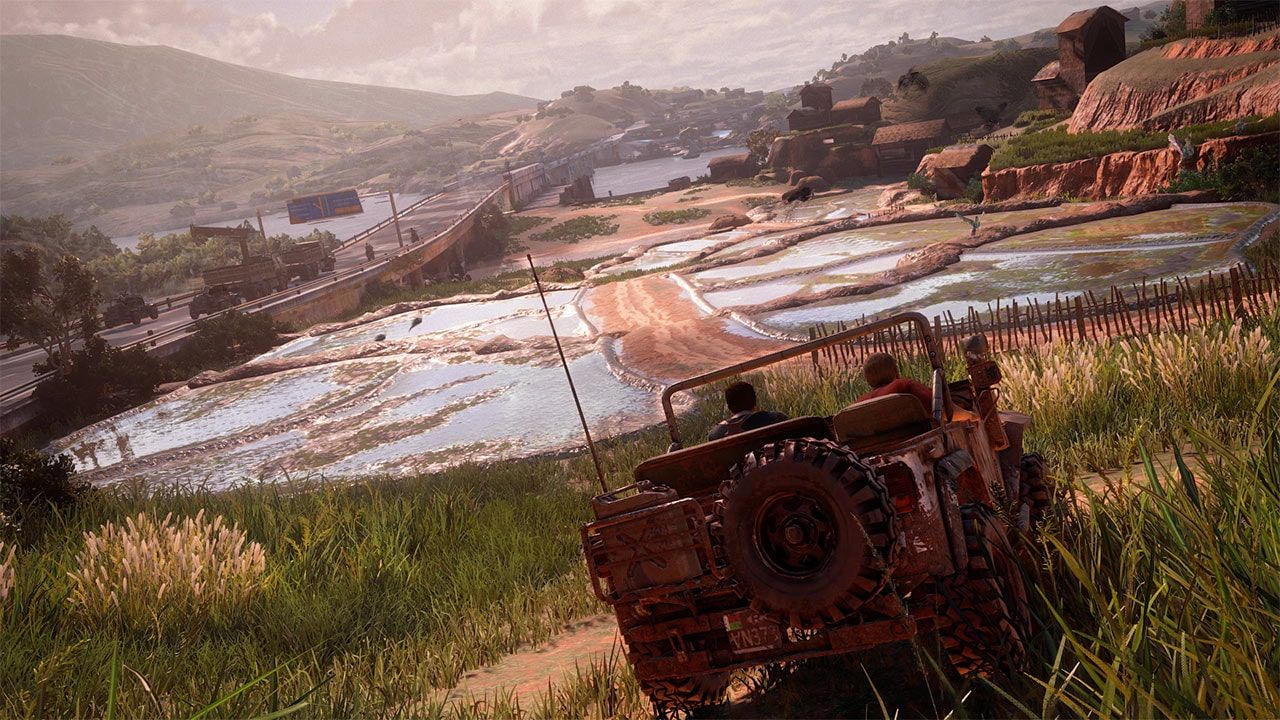 Rear view of a jeep on a grassy slope above a valley and roads.