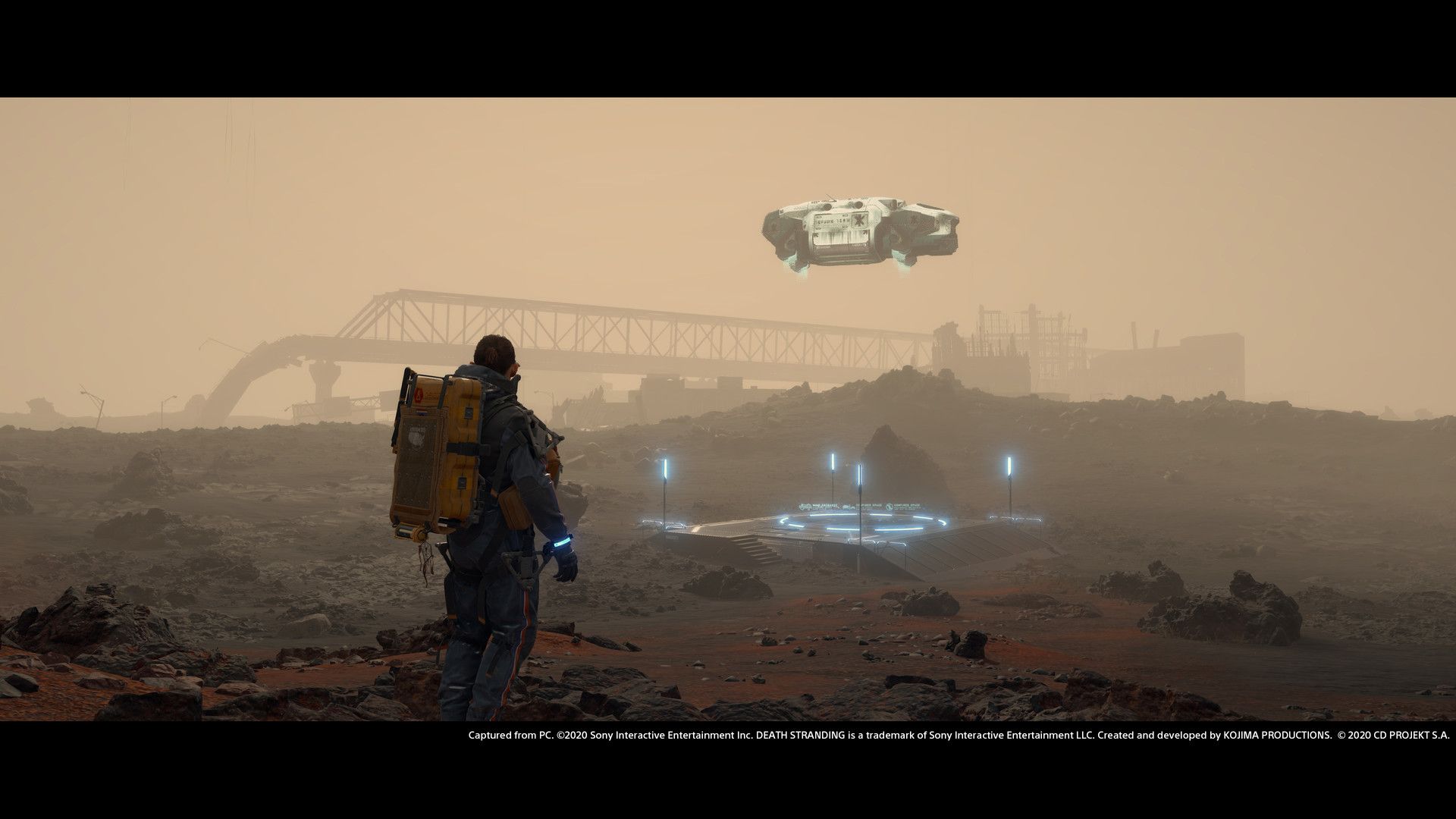 Sam approaches a distant settlement through an orange, dusty landscape.