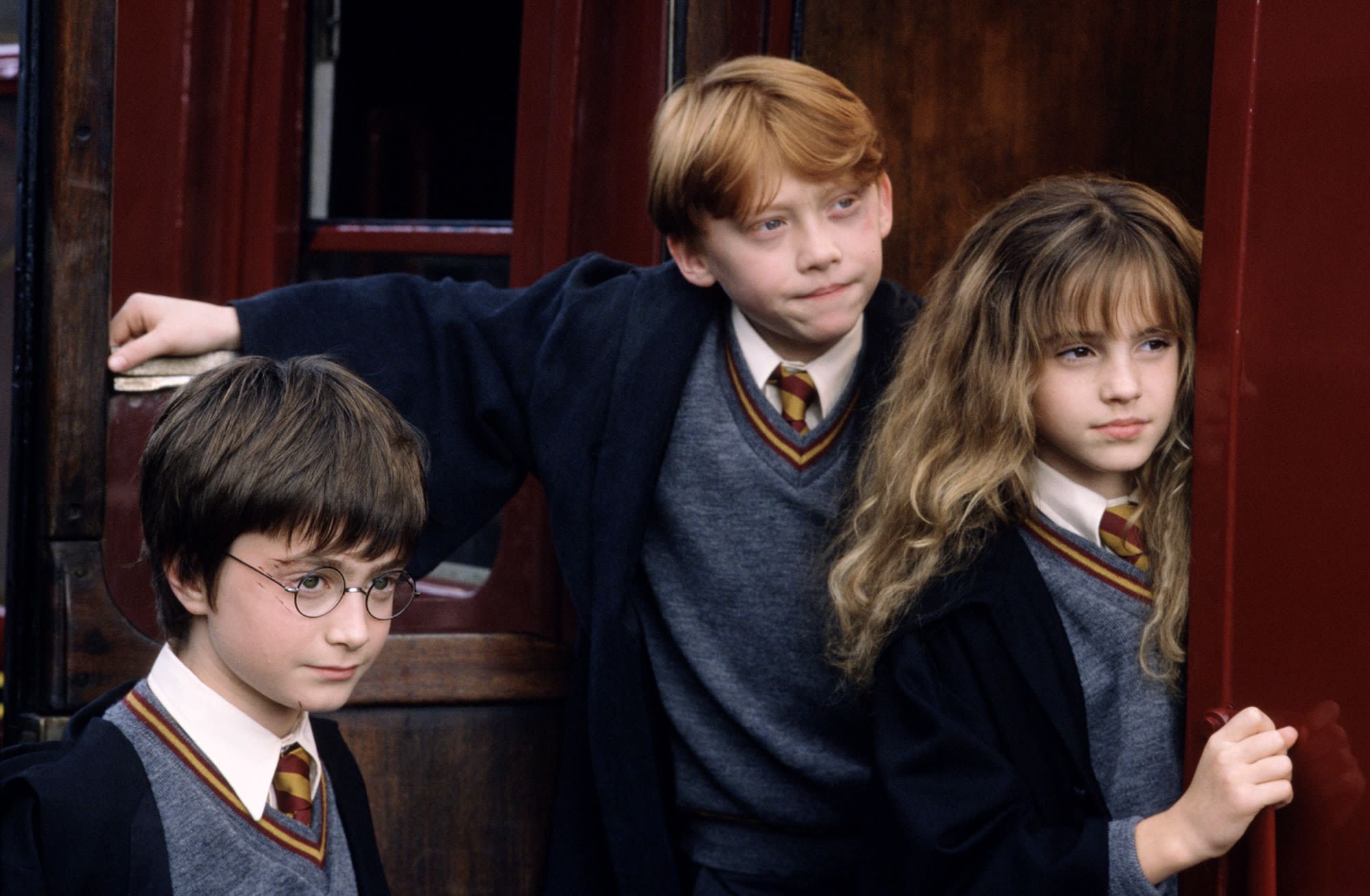 Harry Potter, Ron Weasley, and Hermione Granger beside the Hogwarts Express in official film artwork