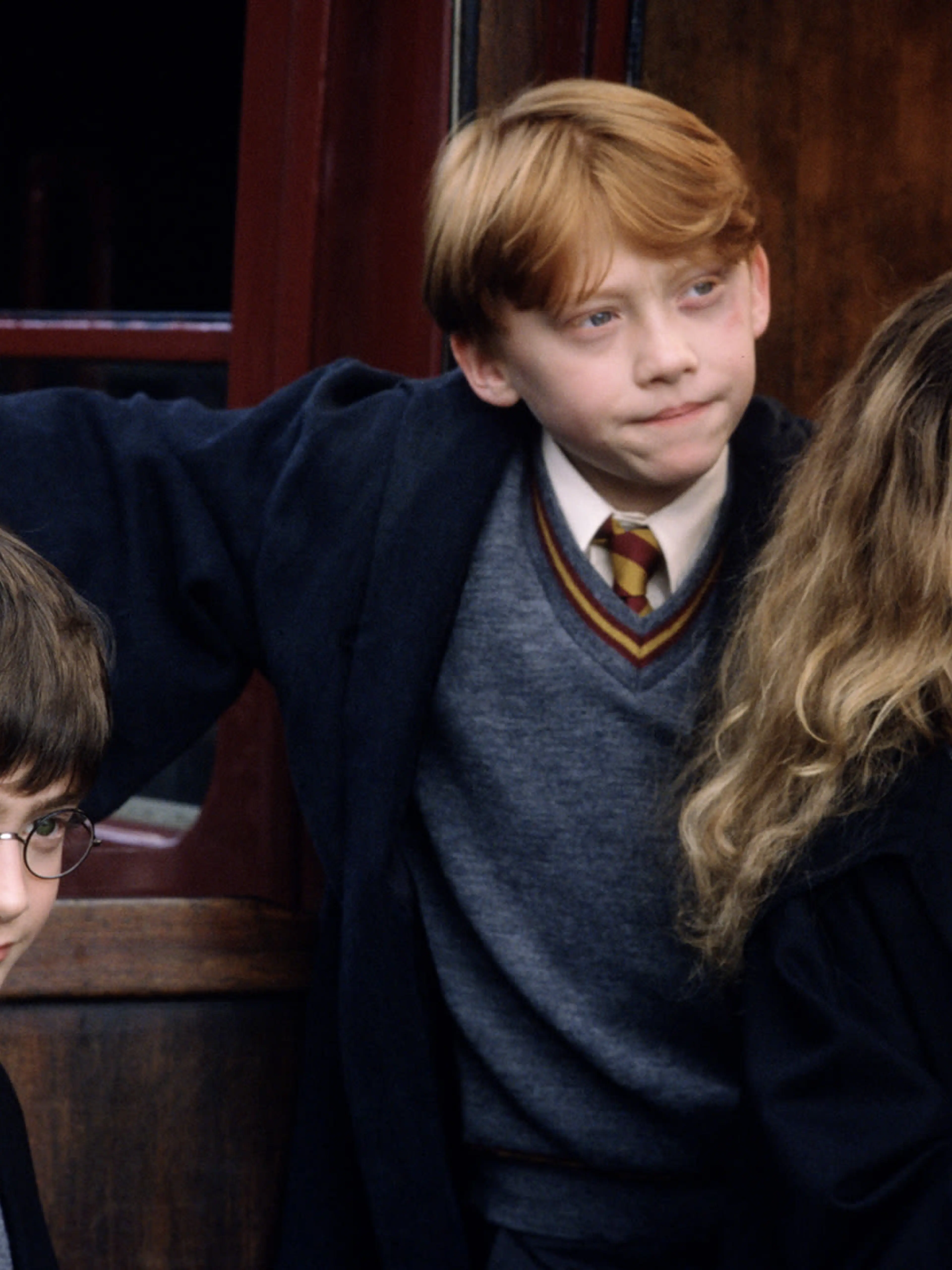 Harry Potter, Ron Weasley, and Hermione Granger beside the Hogwarts Express in official film artwork
