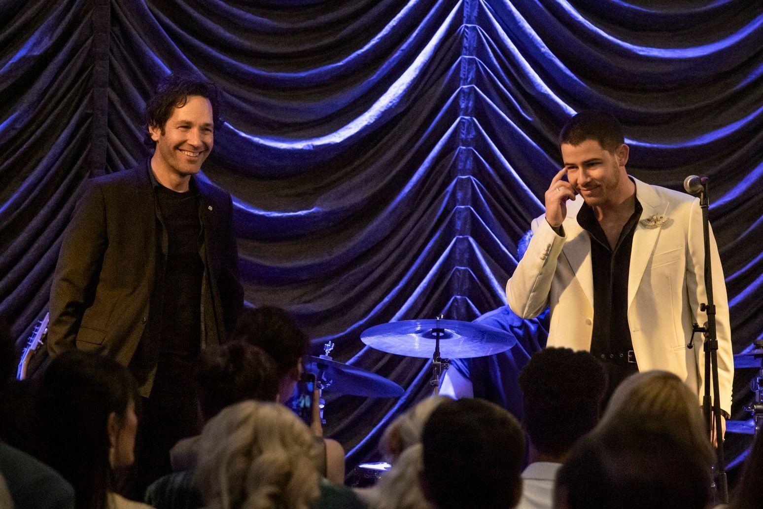 Rick and Danny stand together onstage in front of blue curtains.
