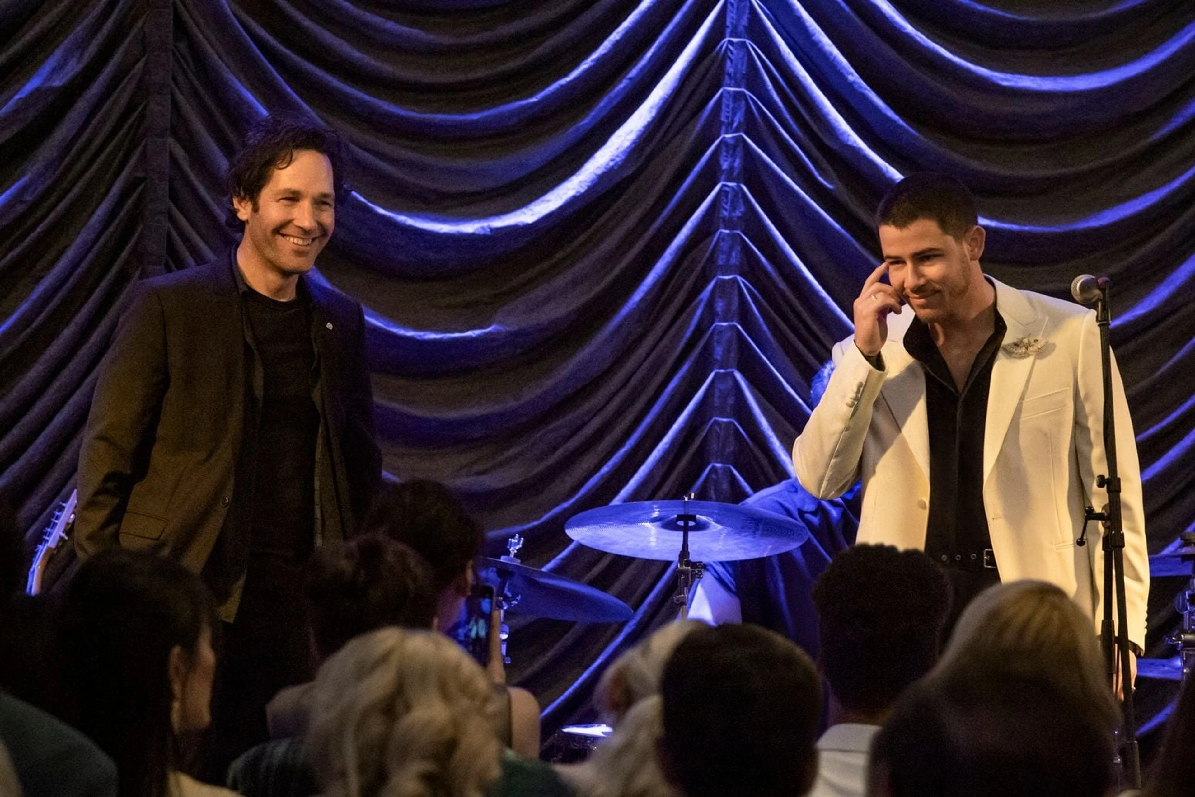 Rick and Danny stand together onstage in front of blue curtains.