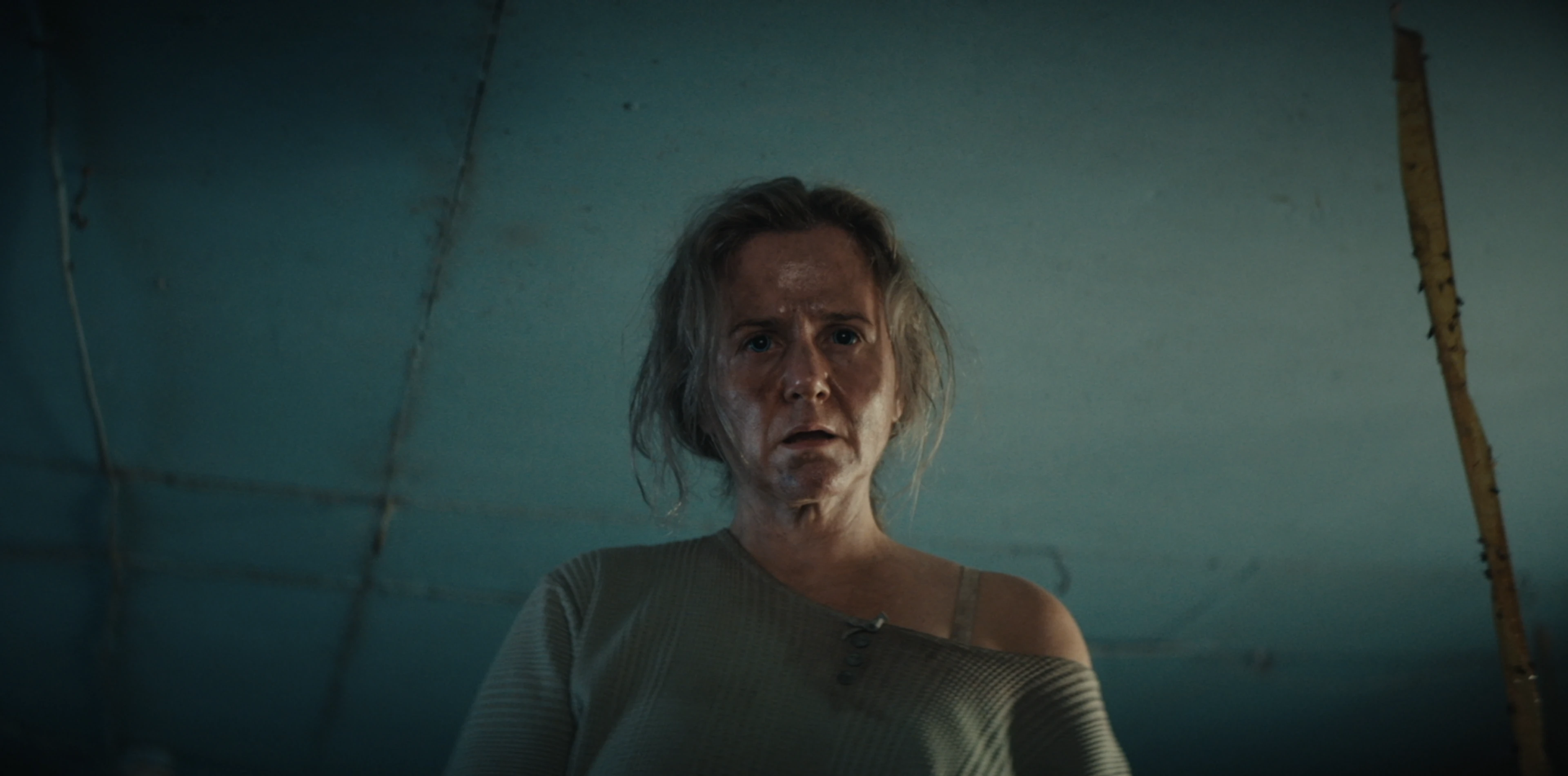 A woman looks downward in a dim room in an official still from Empathie.